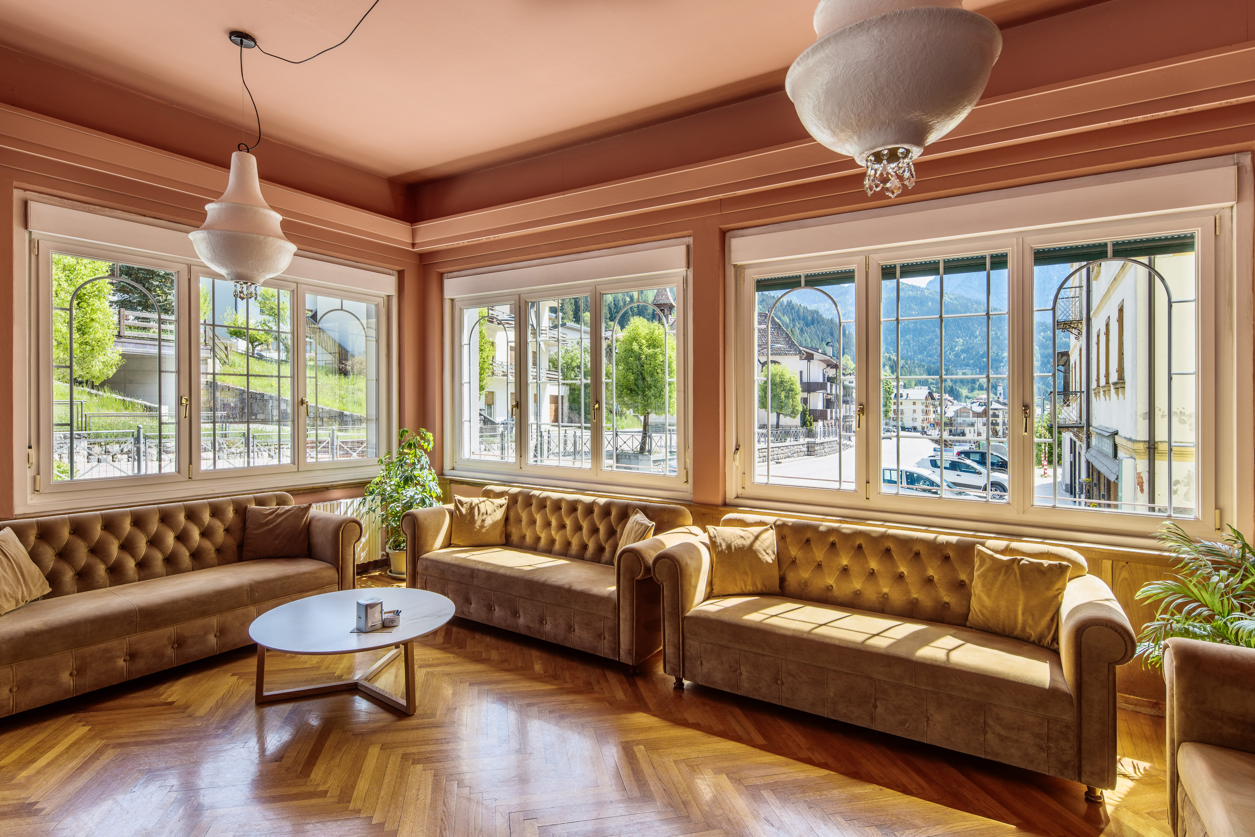 Sunlit living room with brown sofas, herringbone floor, mountain village views.