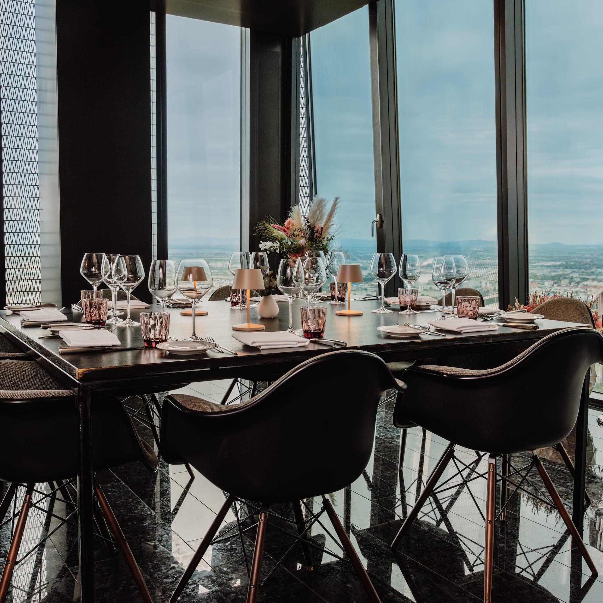 a table with wine glasses and a vase of flowers in front of a window