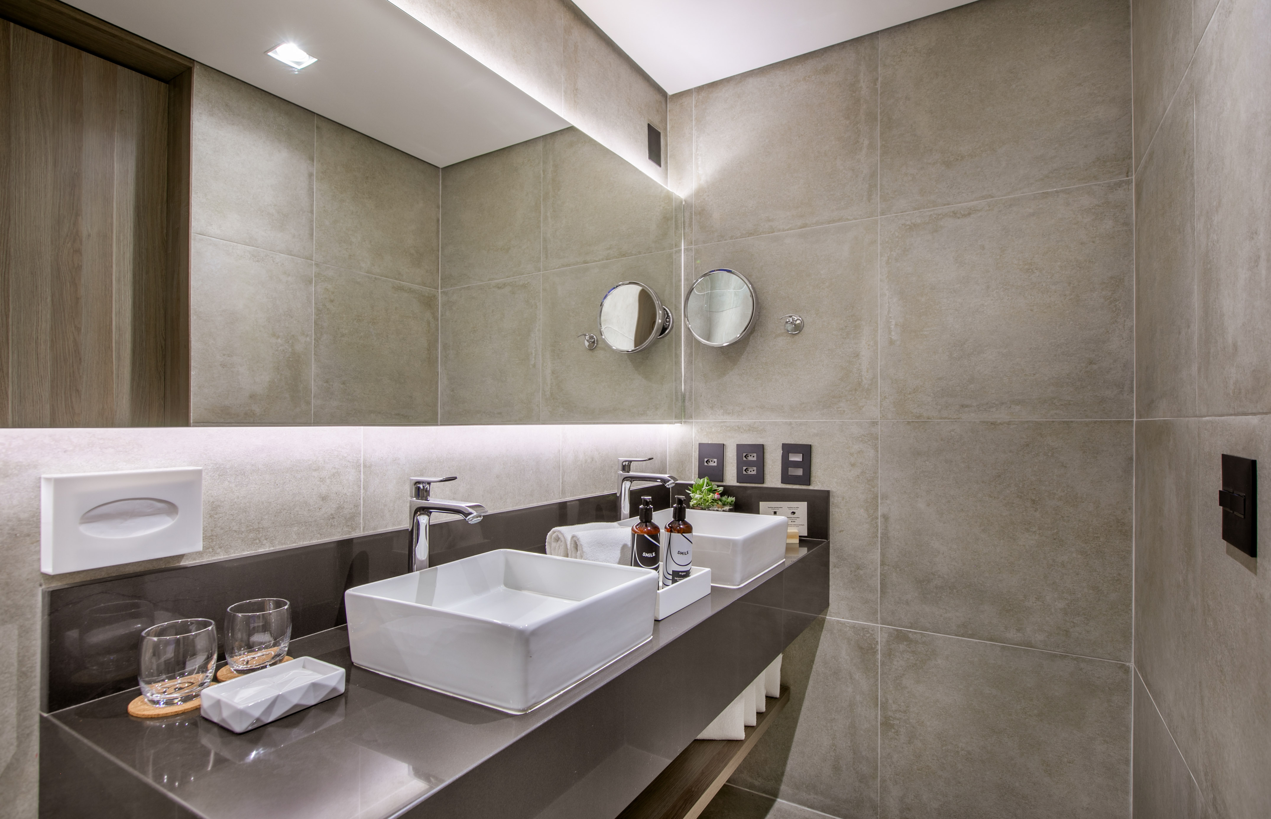 Modern double vanity bathroom with square sinks, backlit mirror, tiled walls.