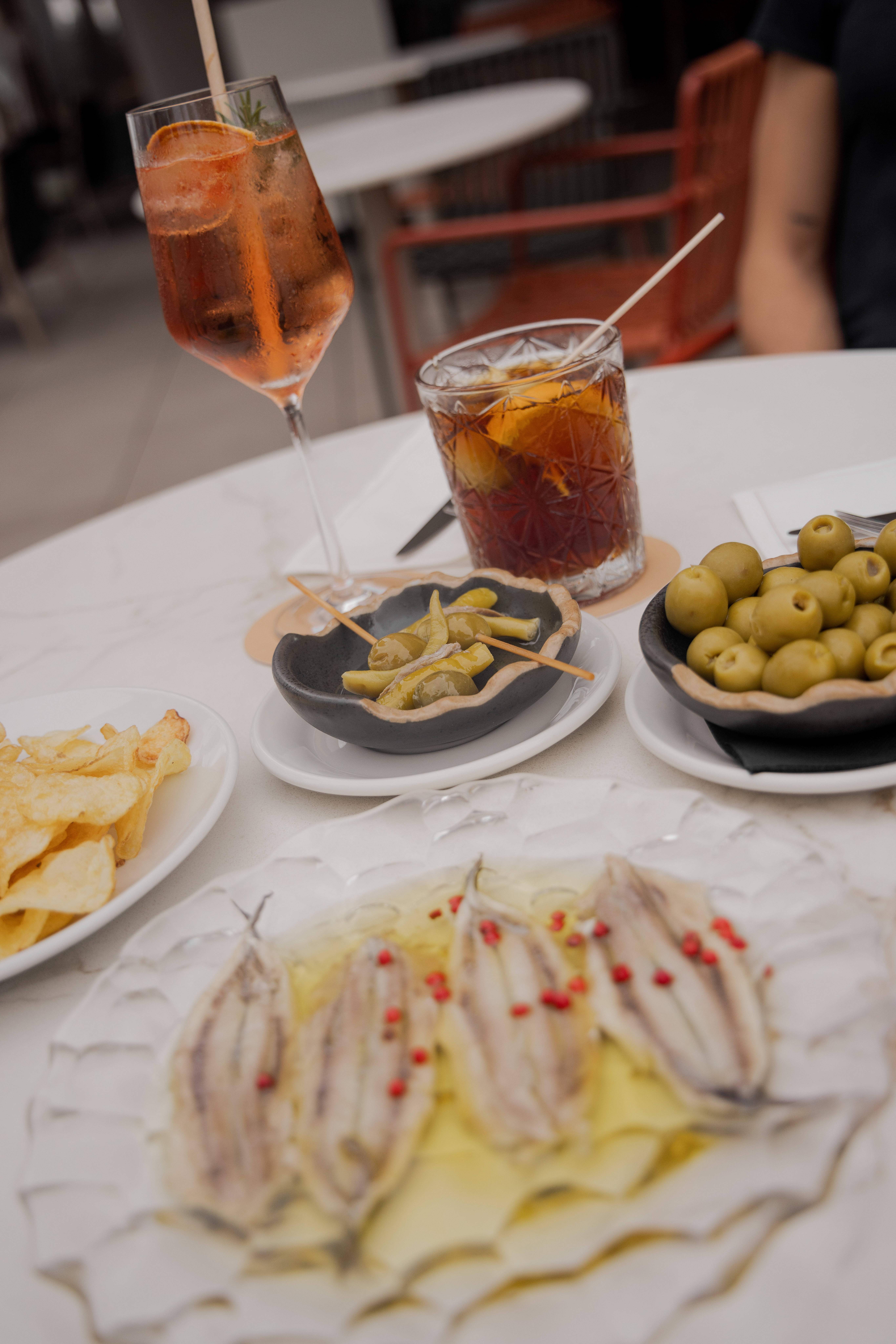 Cocktails with Mediterranean tapas: anchovies, olives, chips, and pickles.