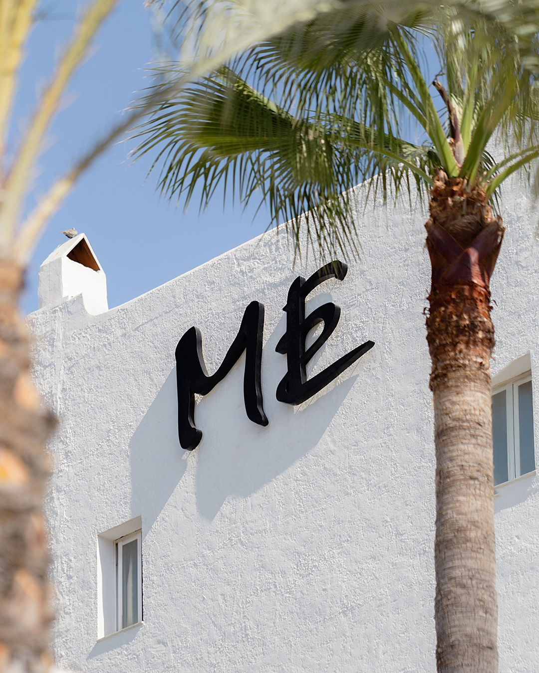 "ME" hotel sign on white building, palm trees, blue sky.