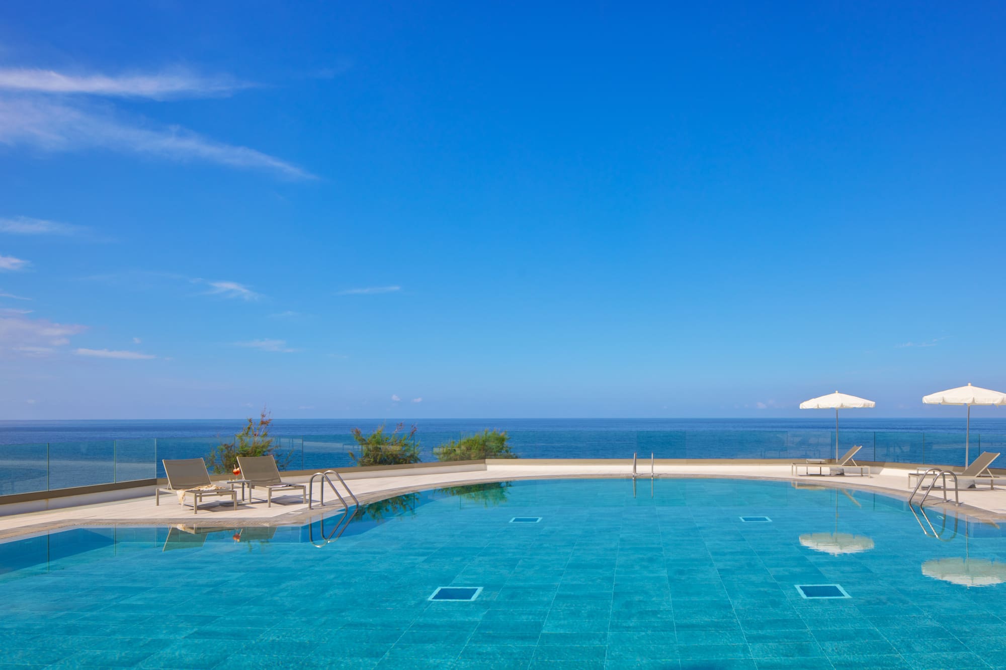 Resort infinity pool with ocean view, lounge chairs, and blue sky.