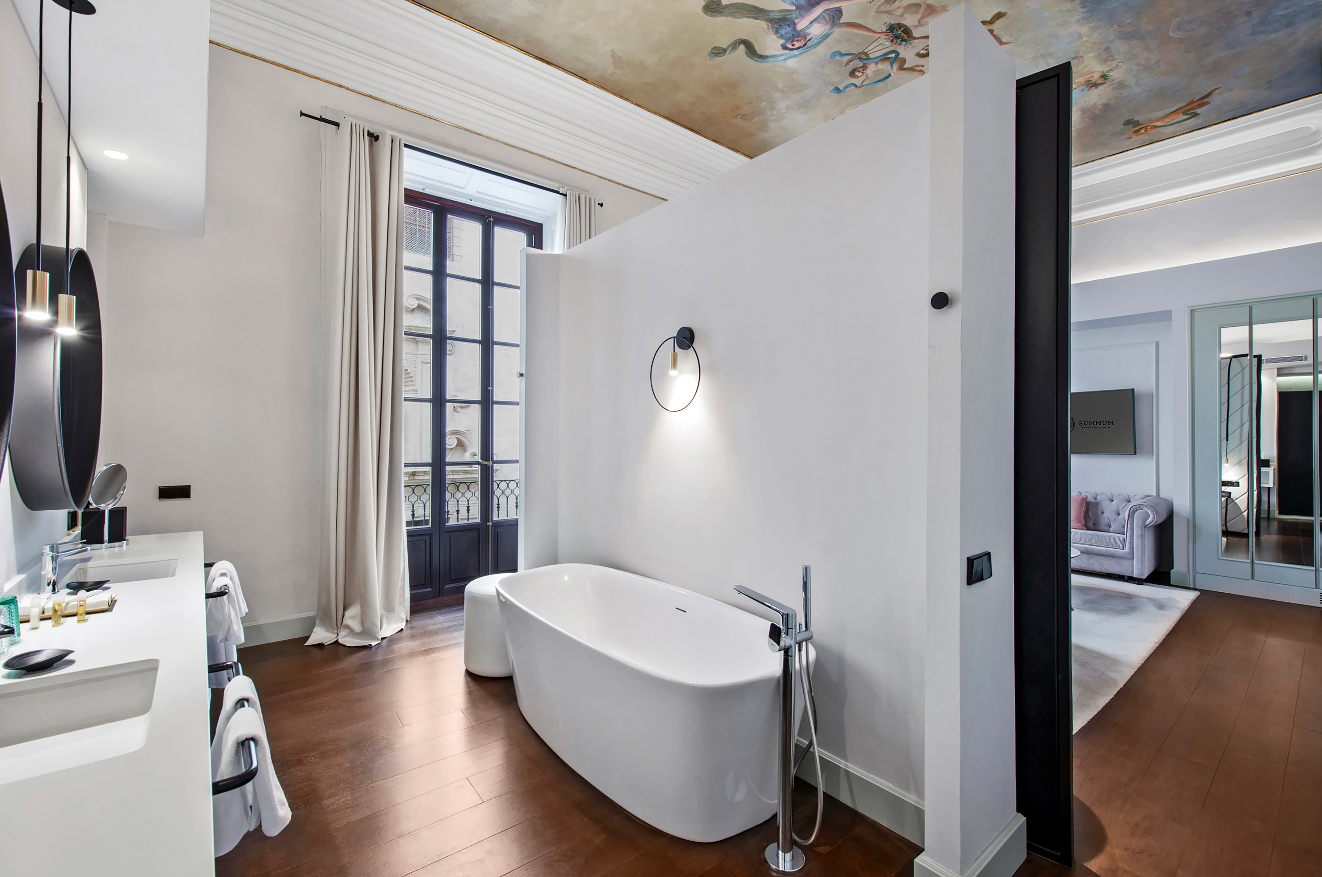 Luxury hotel bathroom with freestanding tub, dual vanity, and fresco ceiling.