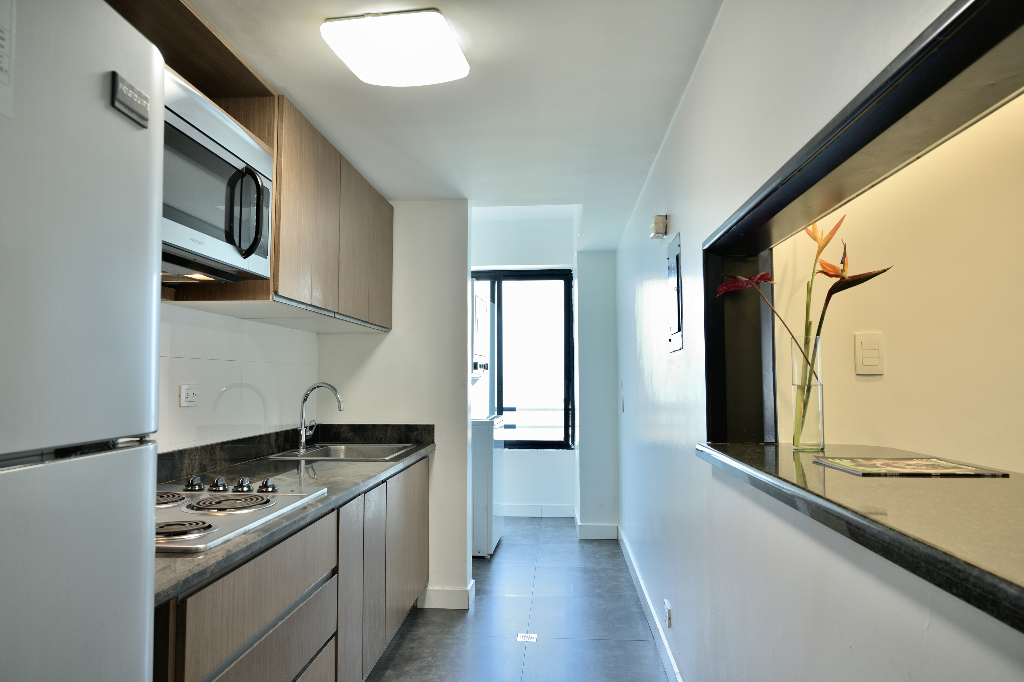 Modern apartment kitchen with white appliances, wood cabinets, dark counters.