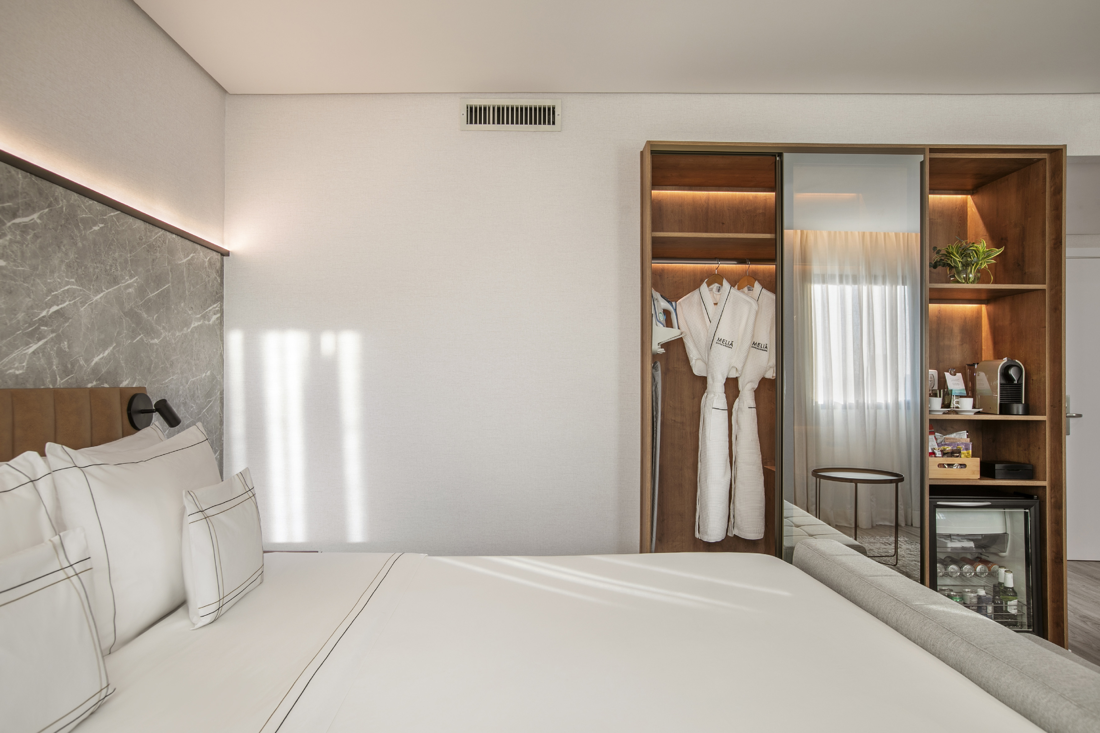 Modern Meliá hotel room with bed, marble accent, wardrobe, and minibar.