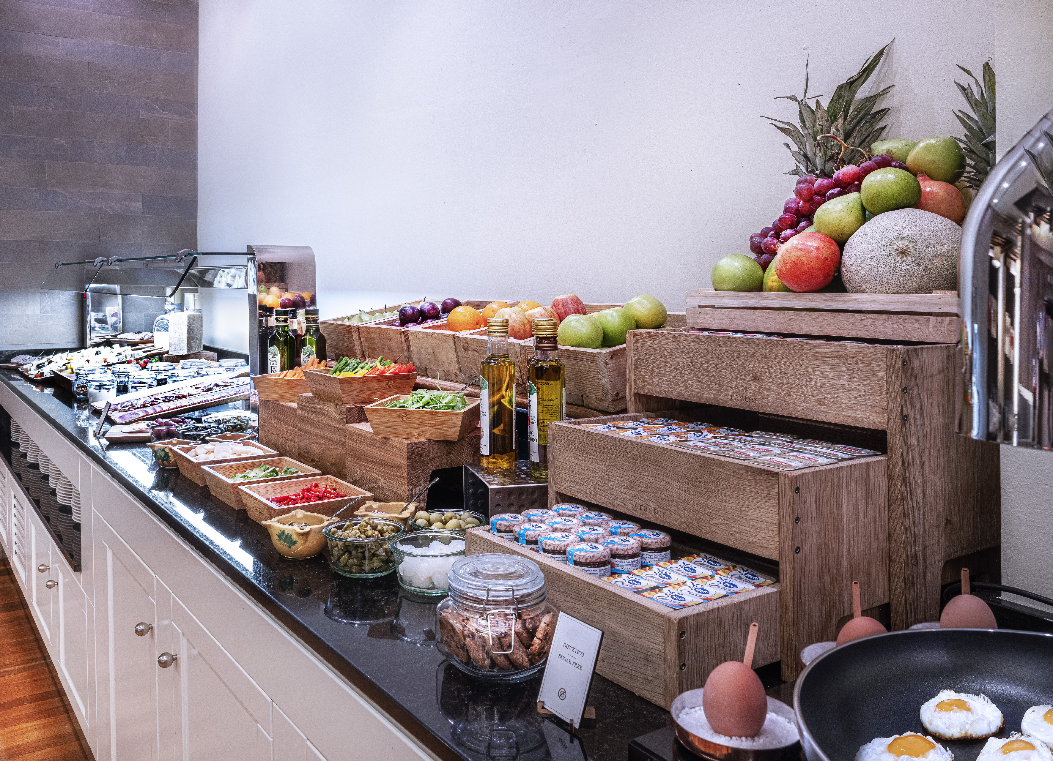 Colorful breakfast buffet with fresh fruit, eggs, vegetables, and olive oil.