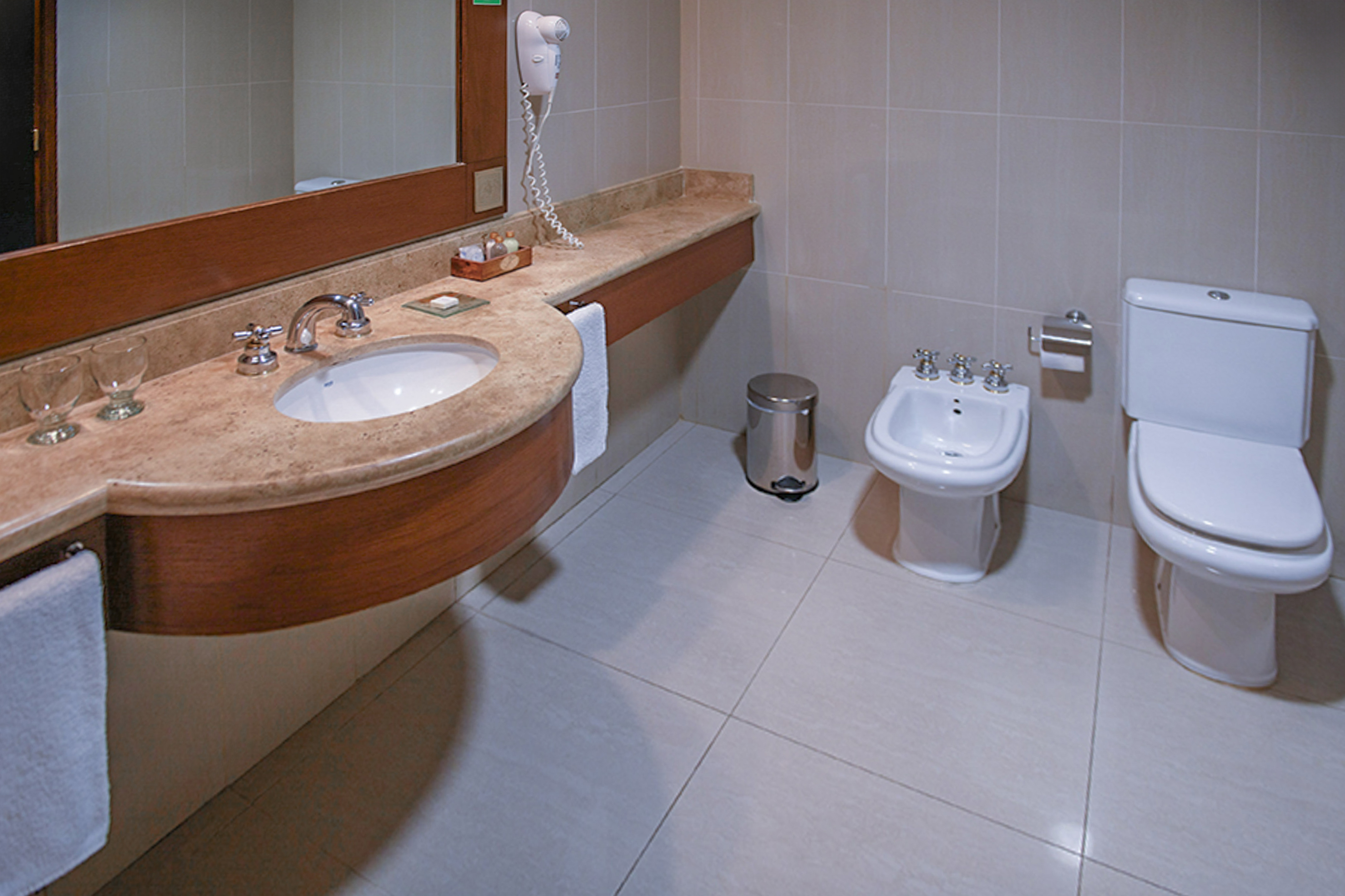 Modern hotel bathroom with marble vanity, sink, mirror, toilet, and bidet.