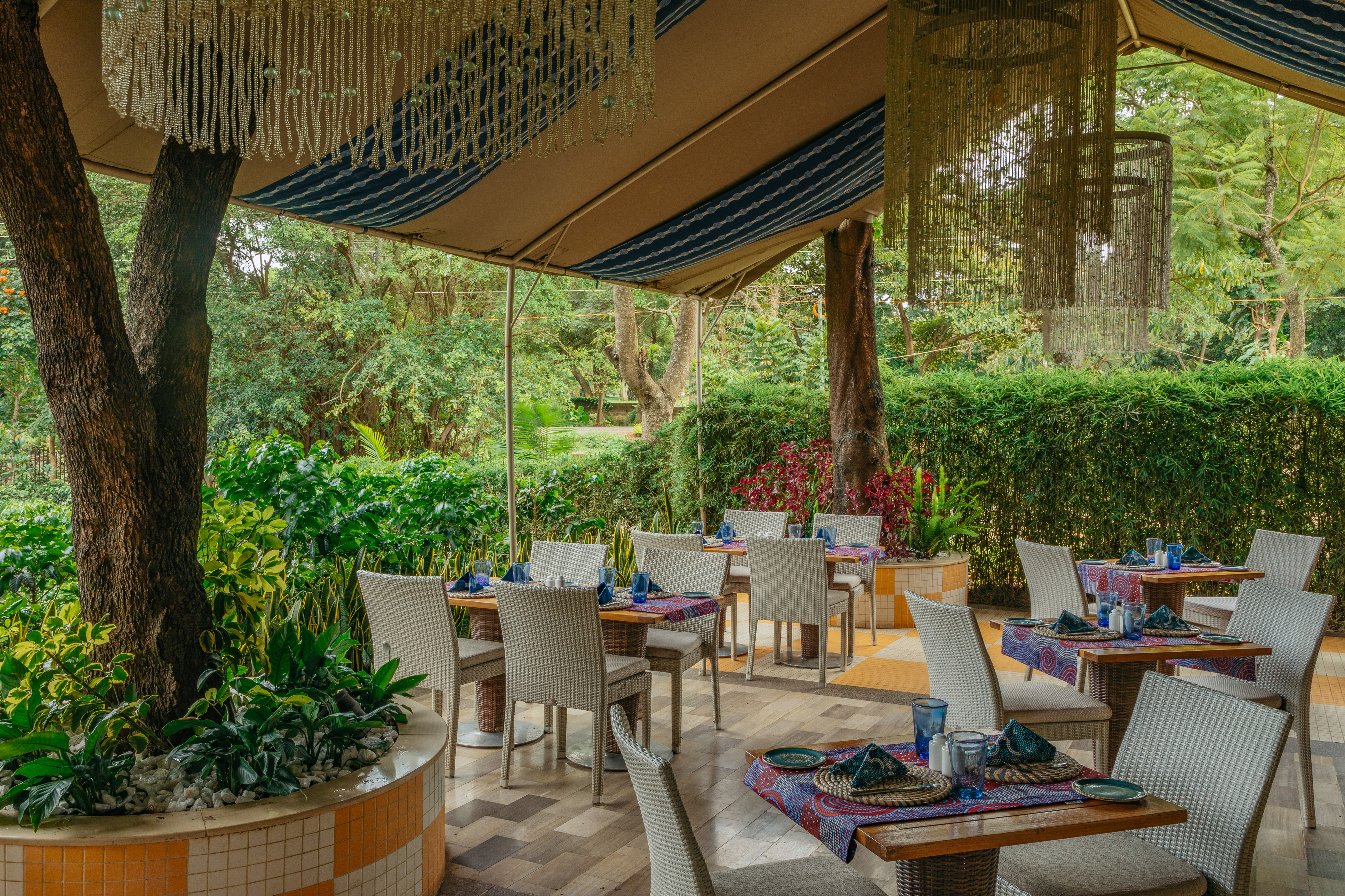 Lush outdoor resort restaurant patio with set tables and decorative canopy.