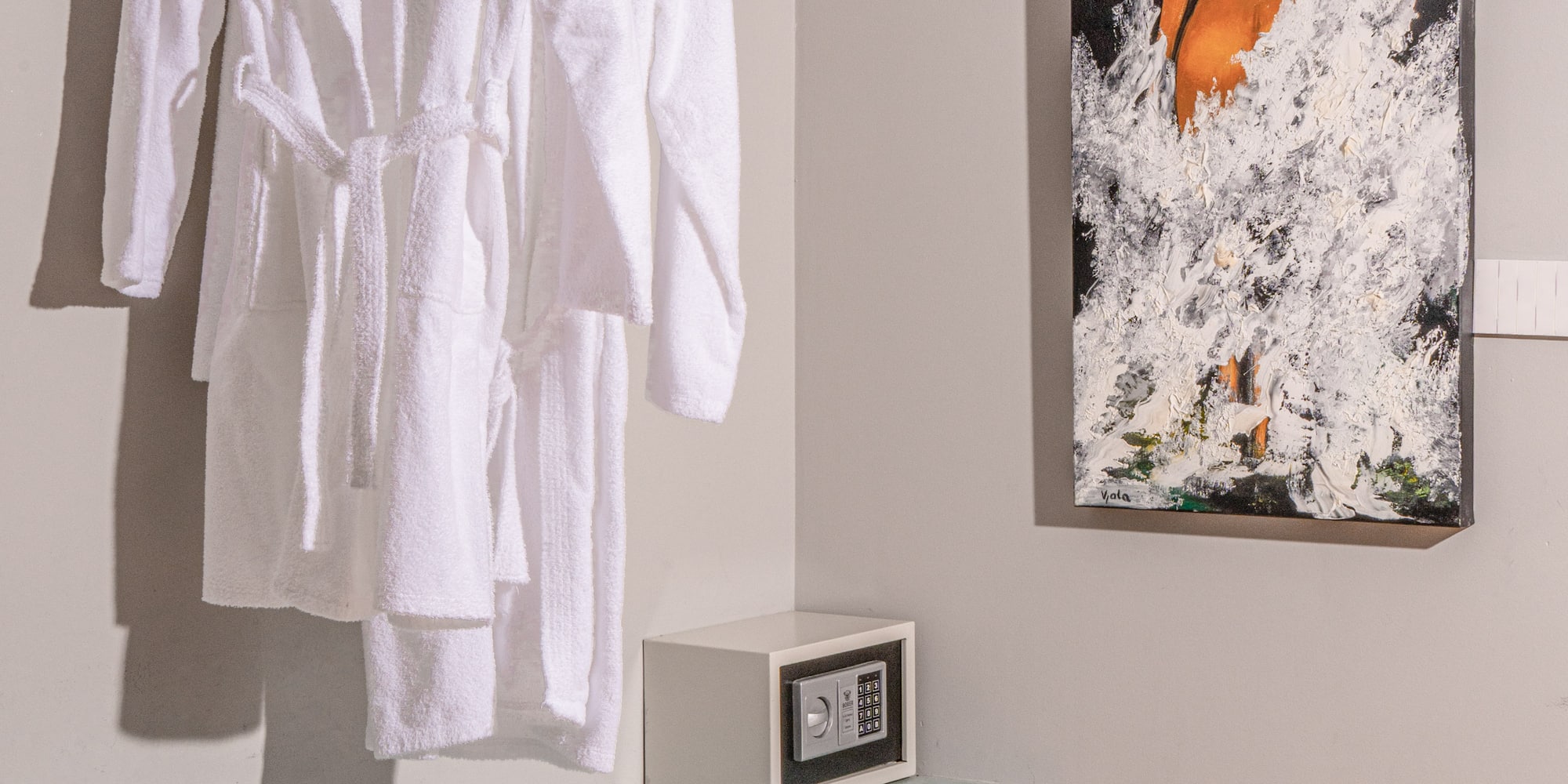 White hotel bathrobes, security safe, and modern art in a guest room.