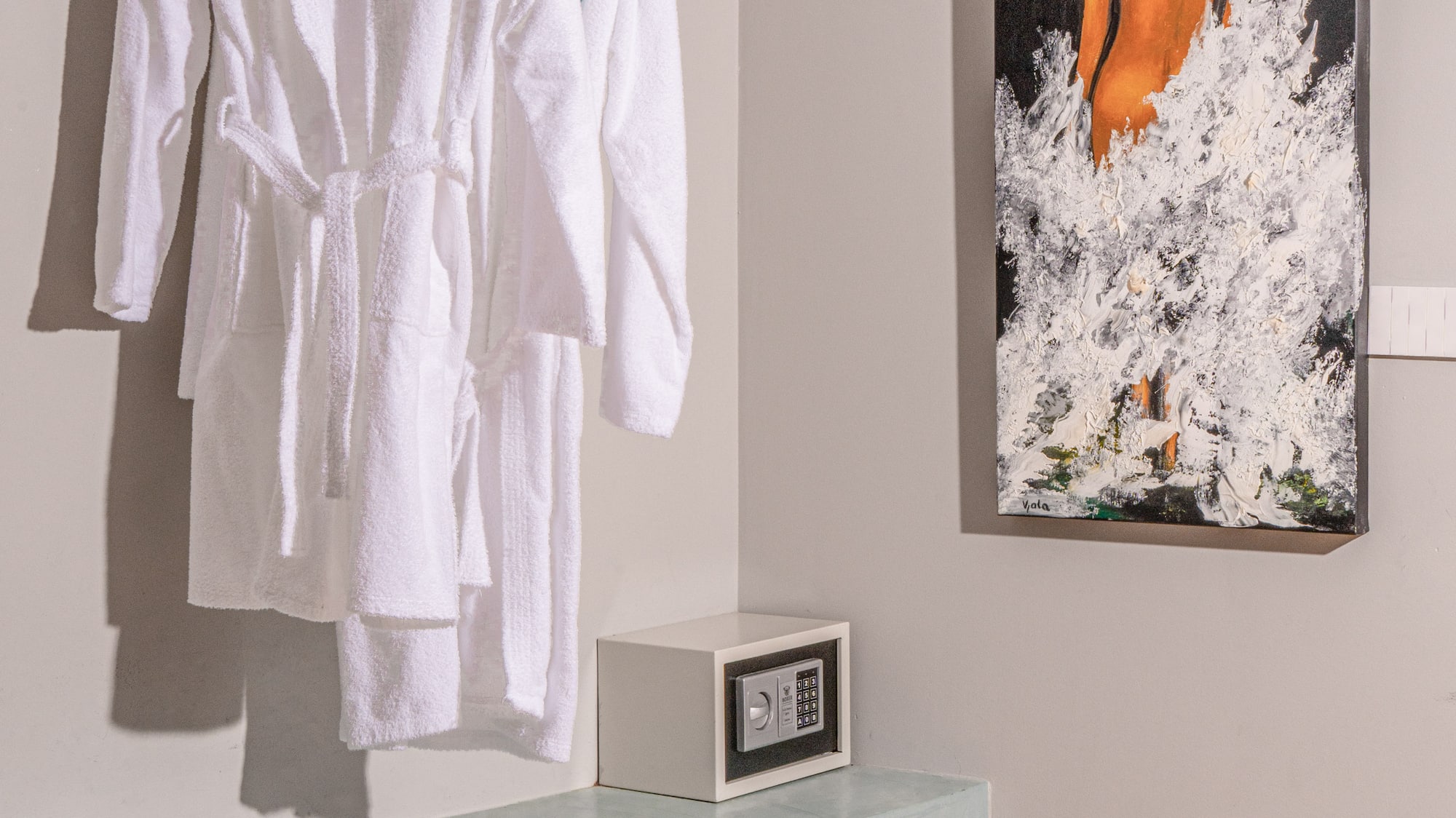 White hotel bathrobes, security safe, and modern art in a guest room.