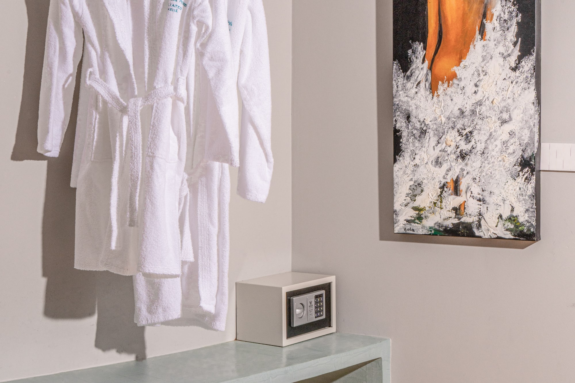 White hotel bathrobes, security safe, and modern art in a guest room.