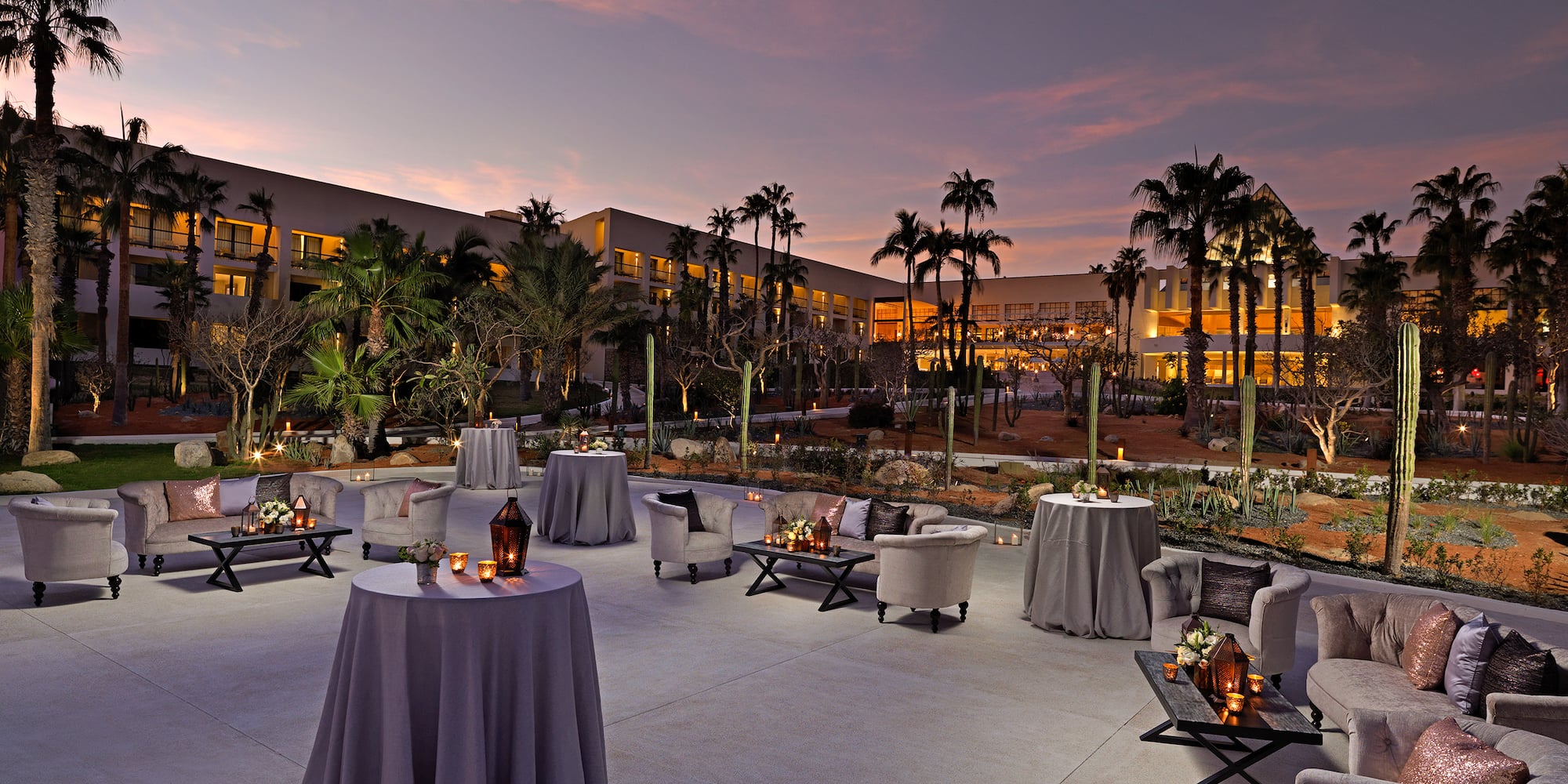 Dusk resort patio with palm trees, elegant lounge seating, and illuminated tables. - Jardín Central - Paradisus Los Cabos - Adults Only, Los Cabos