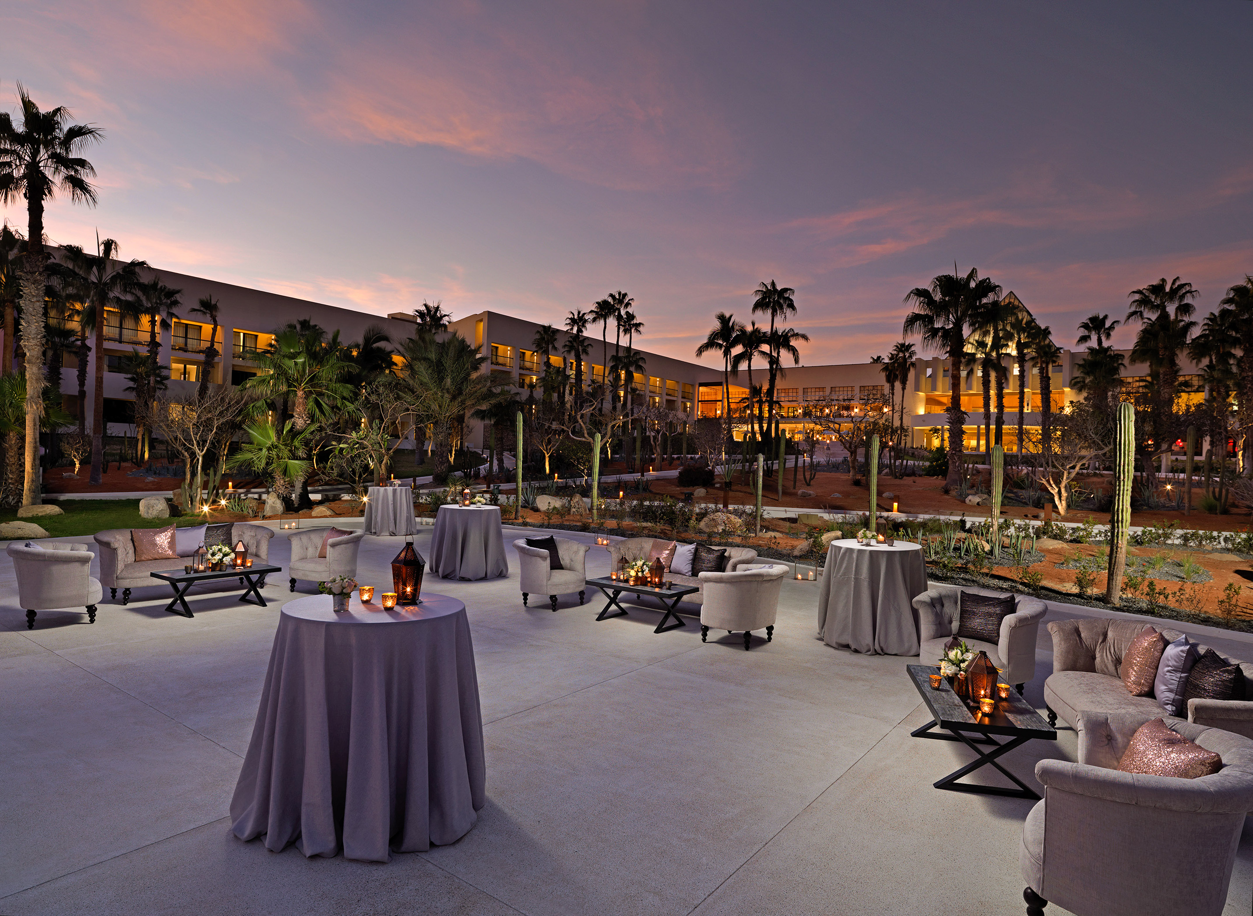Dusk resort patio with palm trees, elegant lounge seating, and illuminated tables. - Jardín Central - Paradisus Los Cabos - Adults Only, Los Cabos