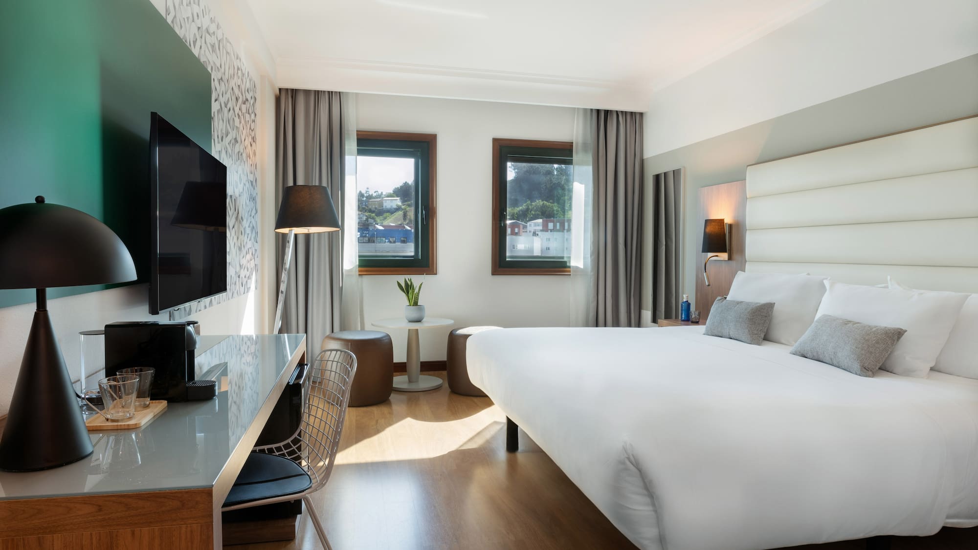 Contemporary hotel room with large bed, desk, TV, and scenic windows.