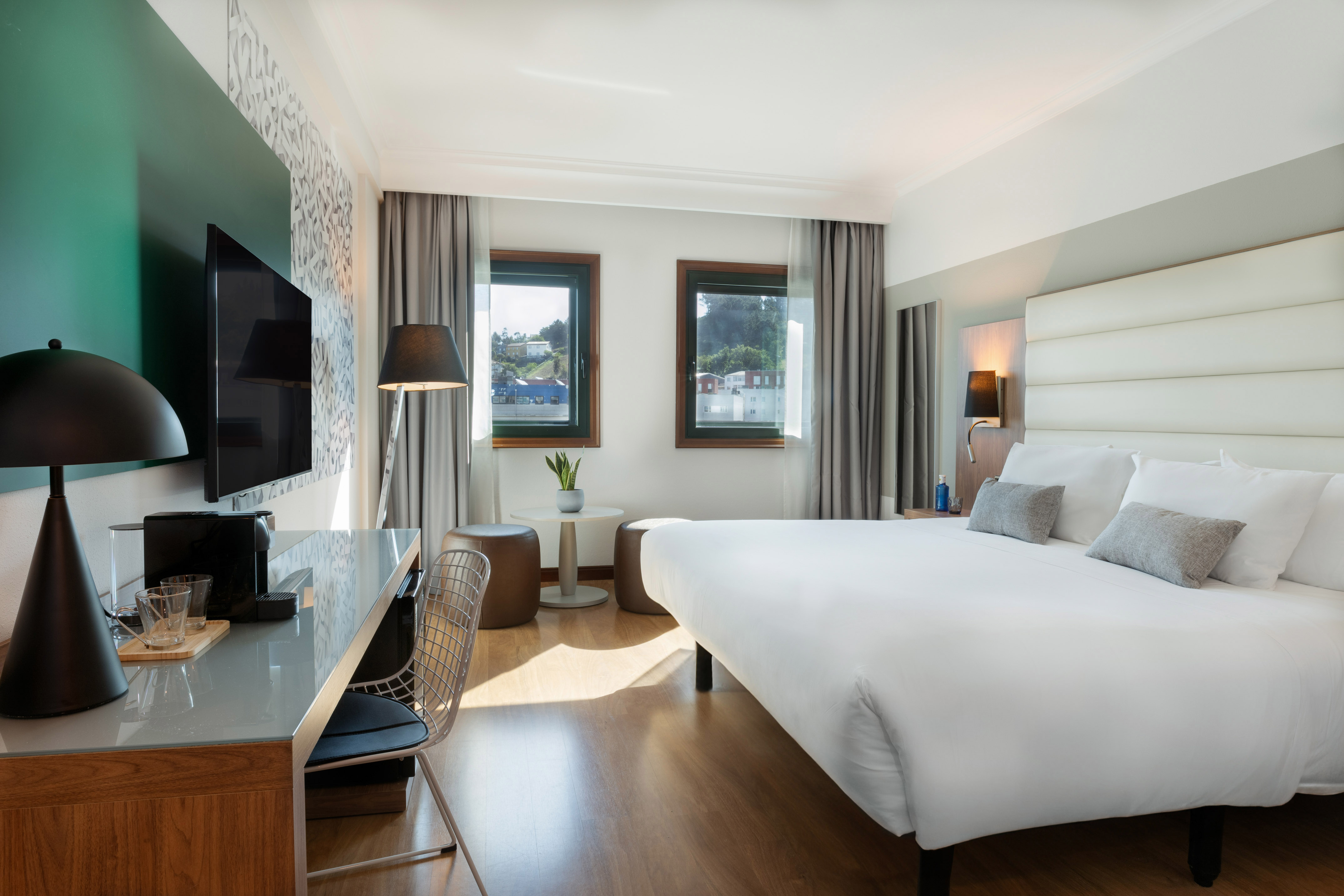 Contemporary hotel room with large bed, desk, TV, and scenic windows.