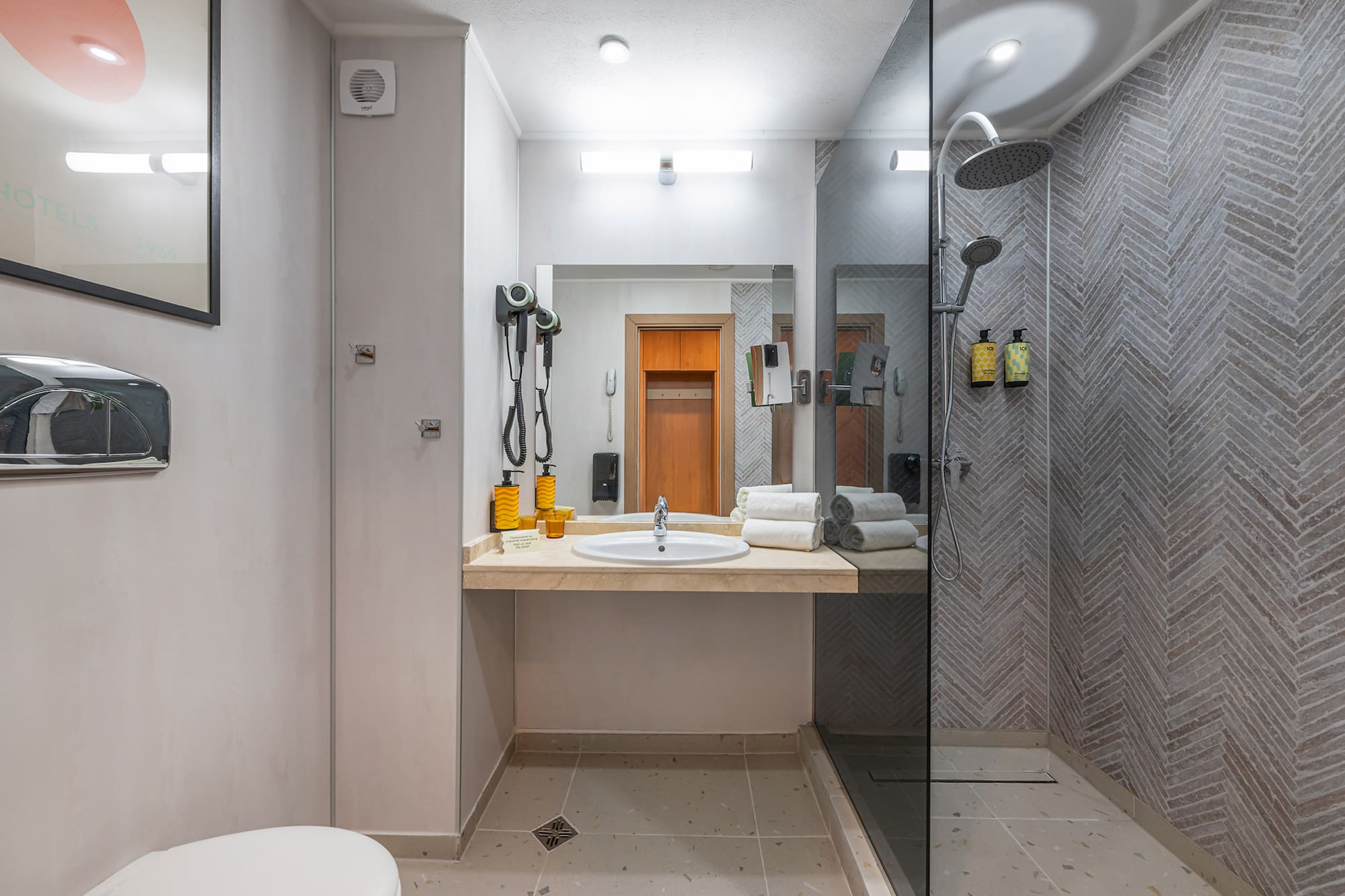 Modern hotel bathroom with vanity, mirror, and shower with herringbone tiles.