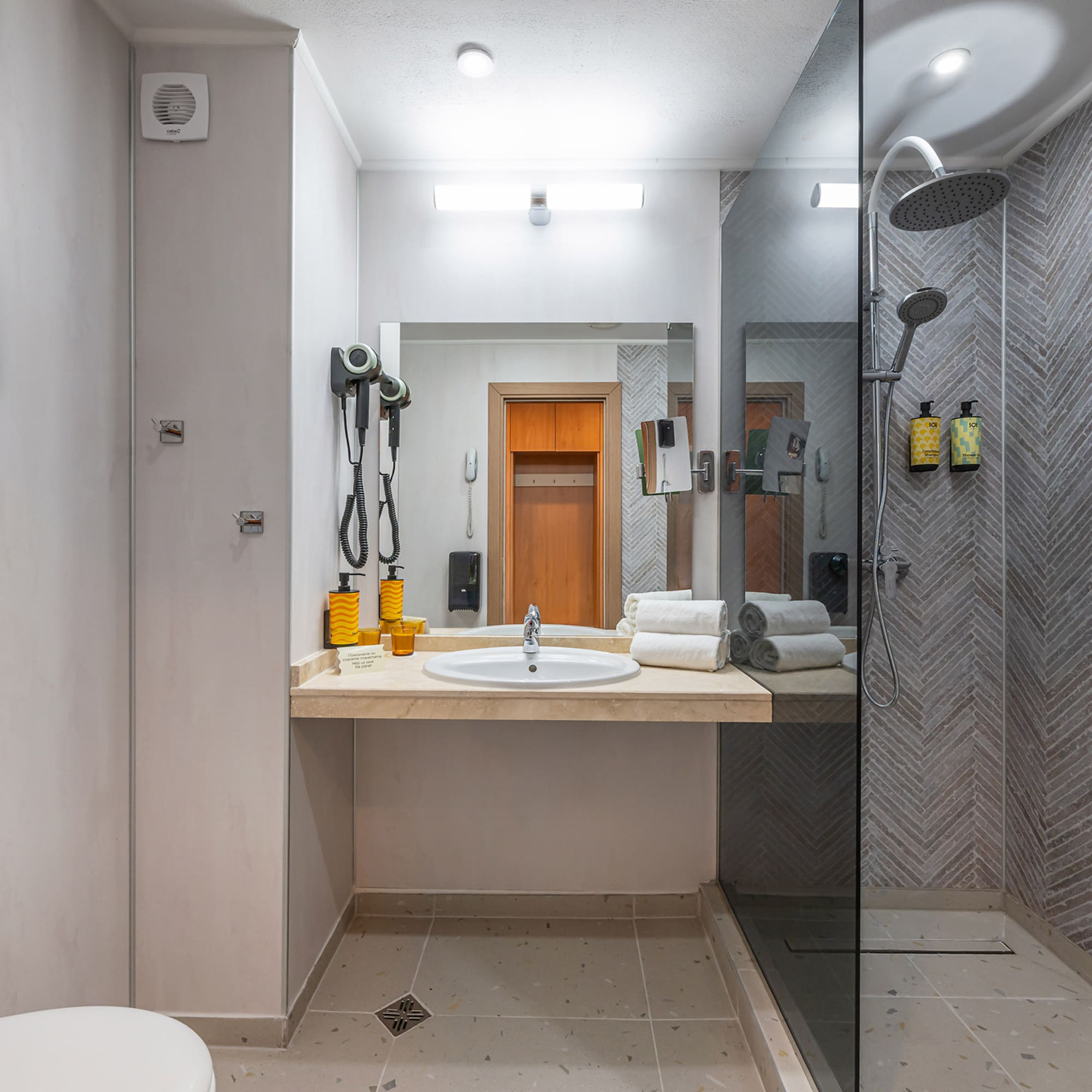 Modern hotel bathroom with vanity, mirror, and shower with herringbone tiles.