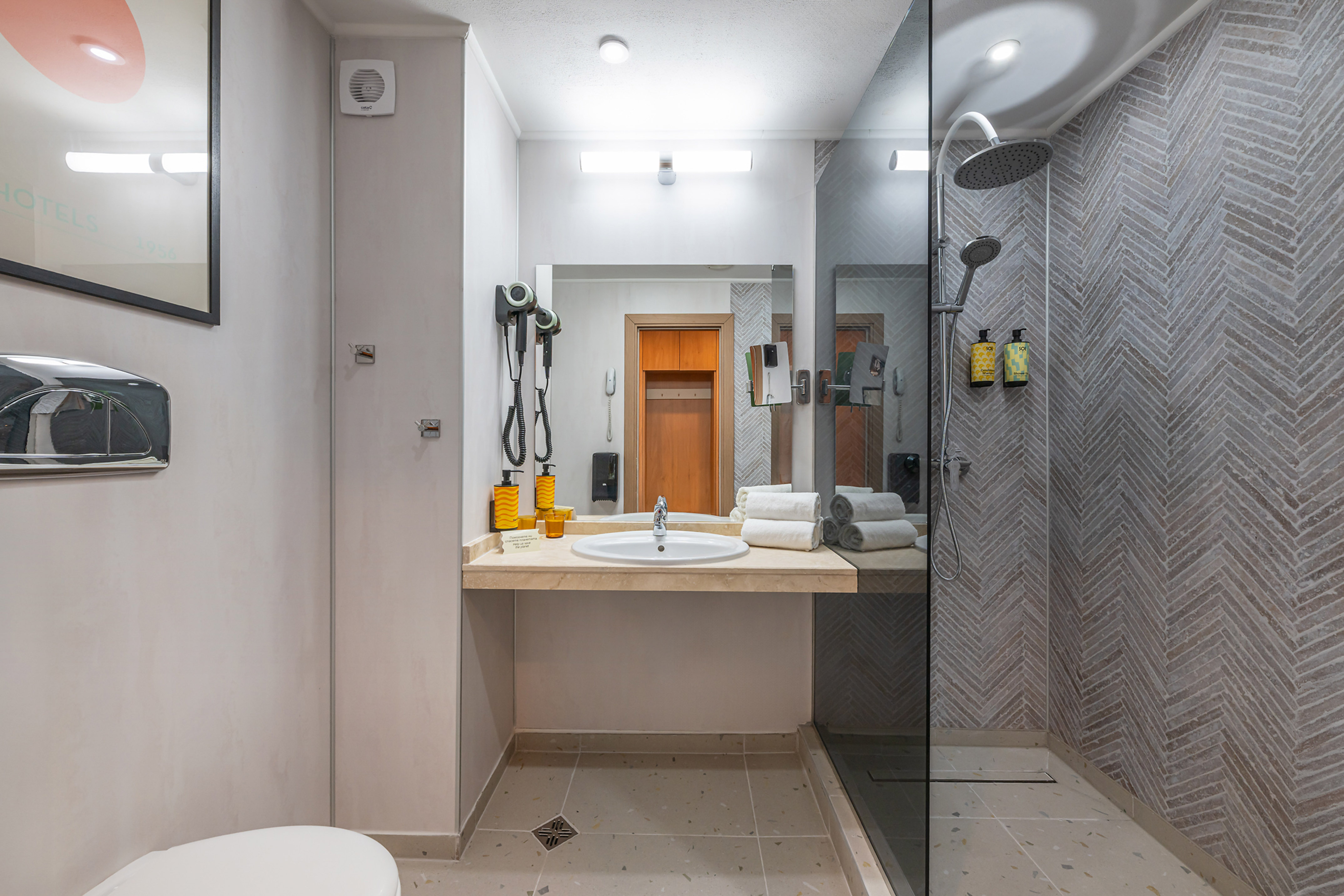 Modern hotel bathroom with vanity, mirror, and shower with herringbone tiles.