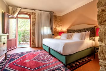 a bed with white sheets and a red rug in a room with a stone wall