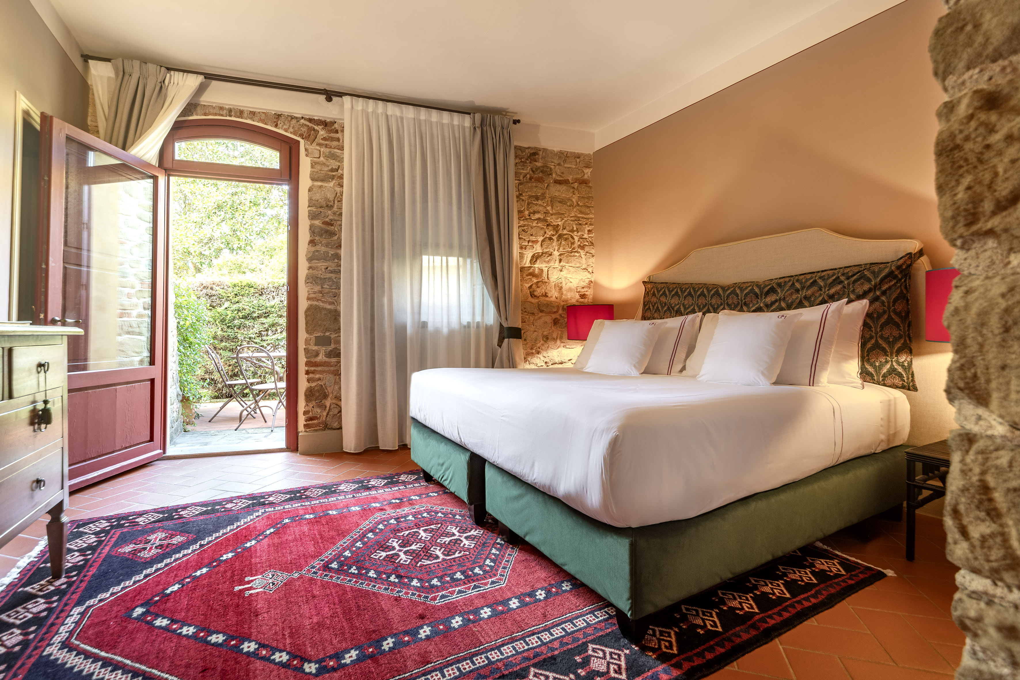 Bedroom with king bed, red rug, stone walls, and open patio door.