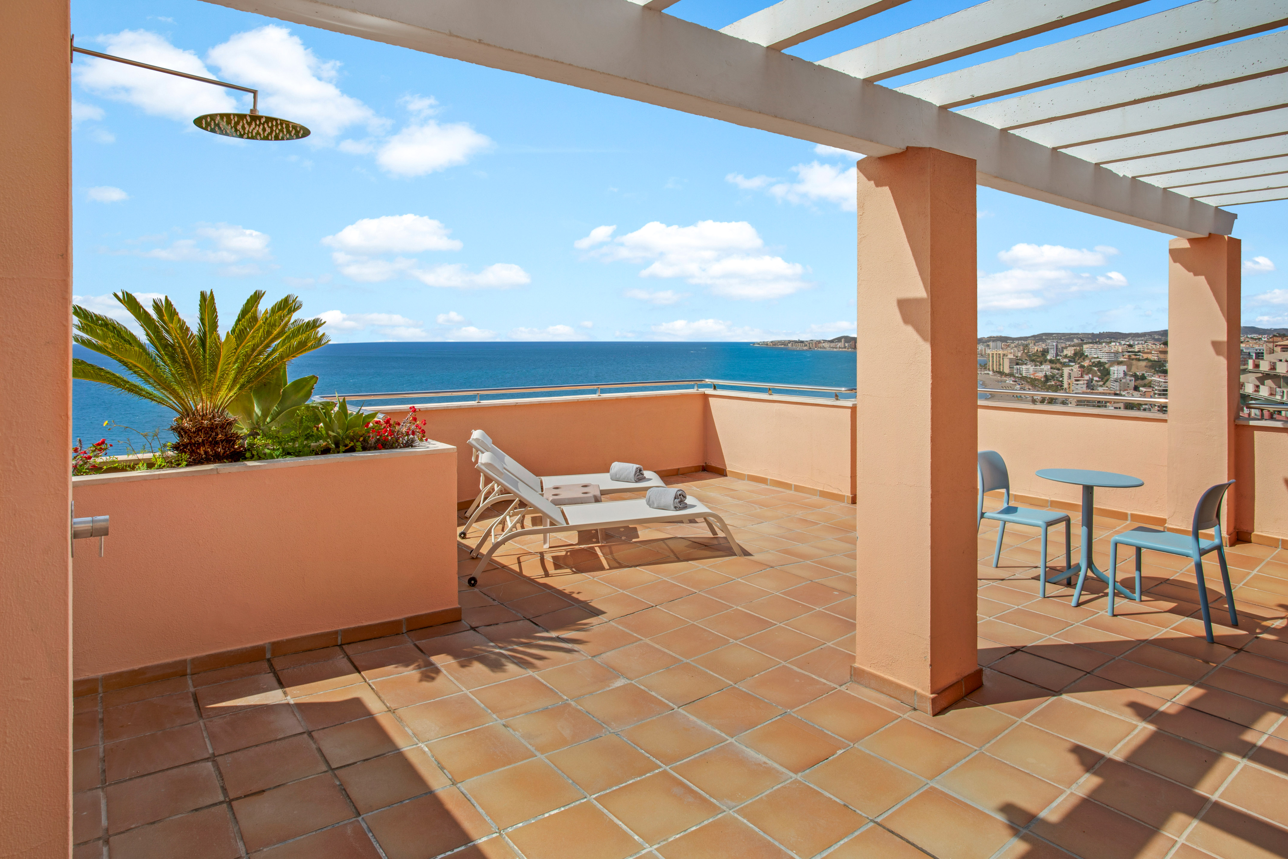 Coastal balcony with ocean view, sun loungers, outdoor shower, and pergola.