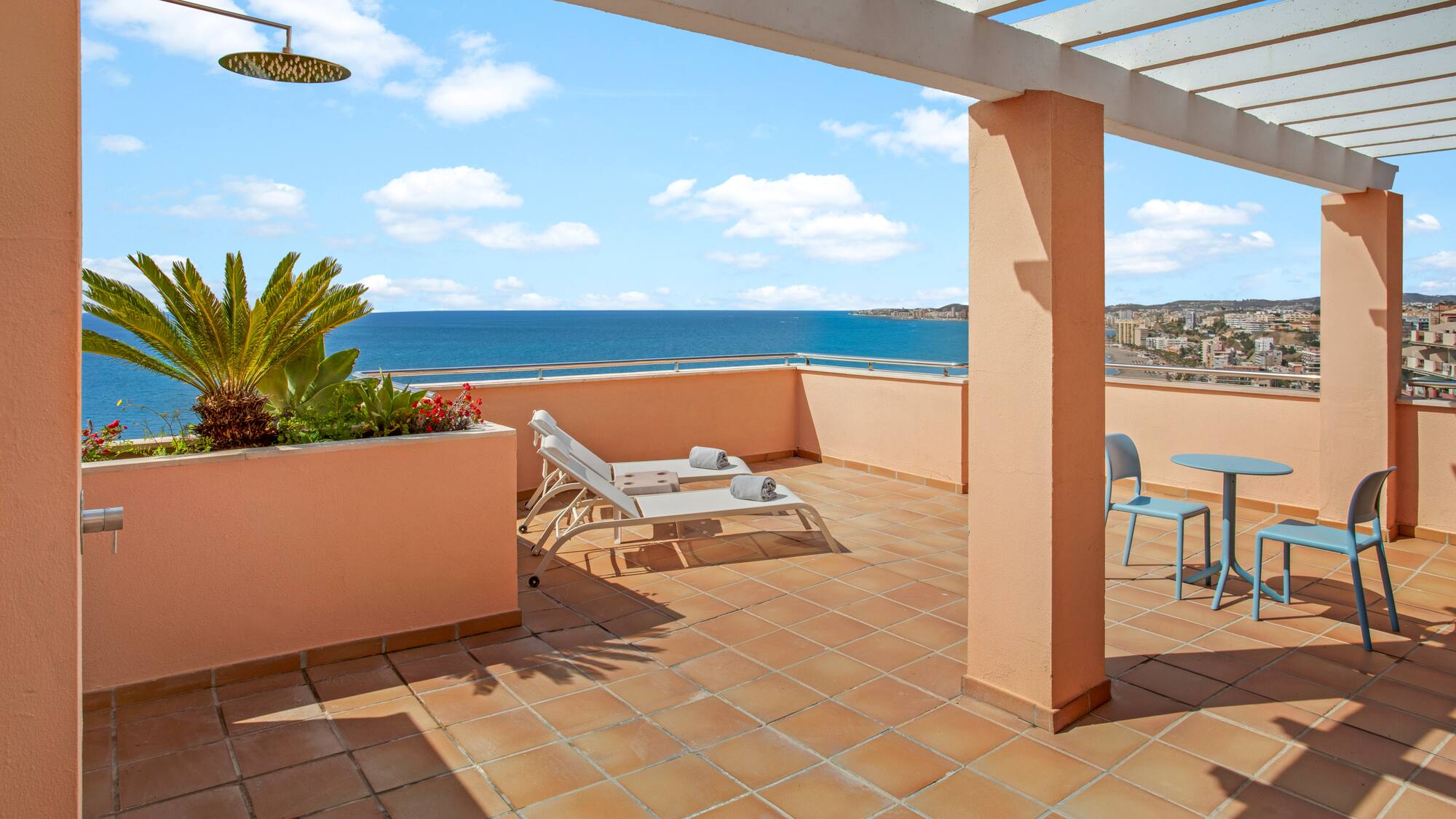 Coastal balcony with ocean view, sun loungers, outdoor shower, and pergola.