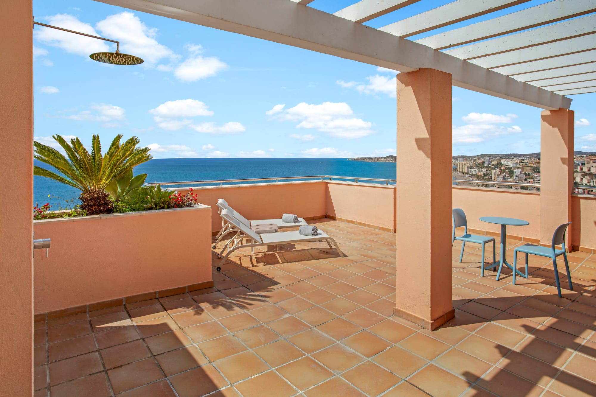 Coastal balcony with ocean view, sun loungers, outdoor shower, and pergola.