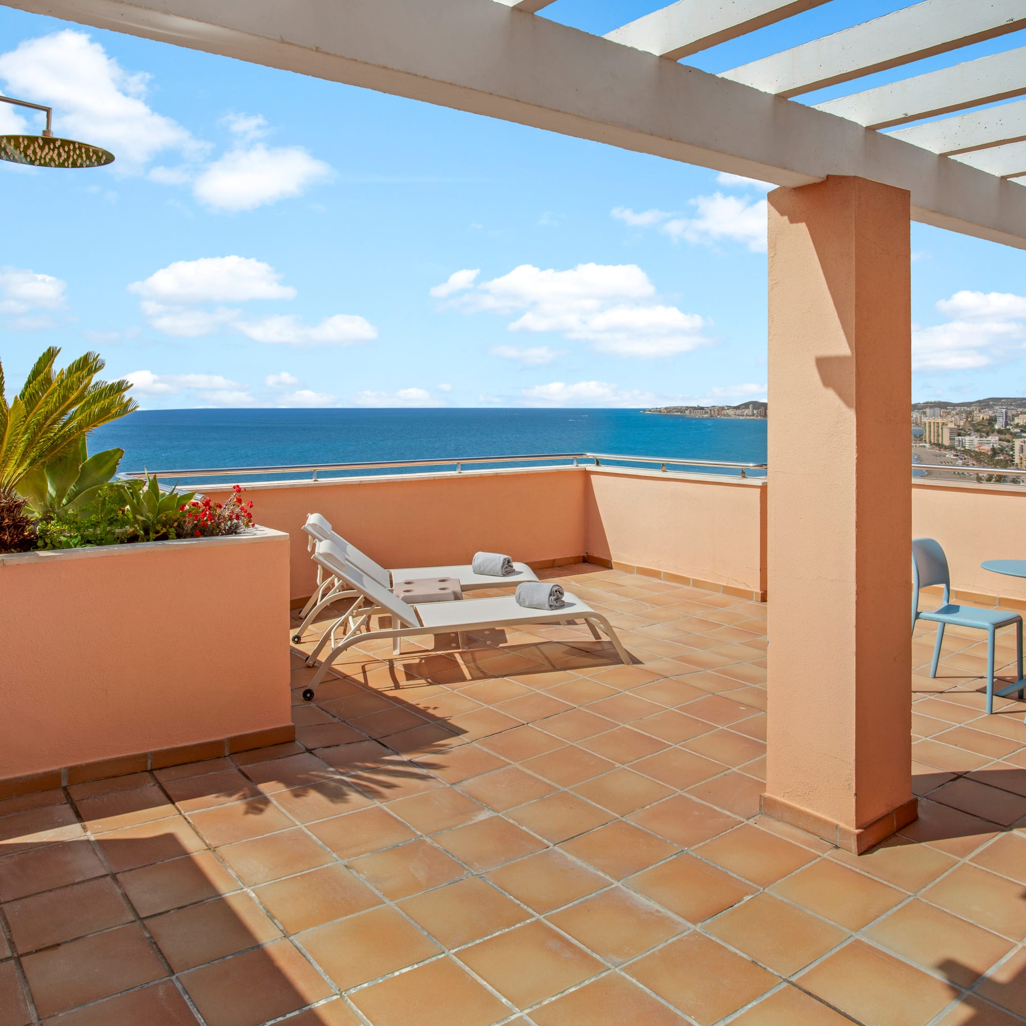 Coastal balcony with ocean view, sun loungers, outdoor shower, and pergola.