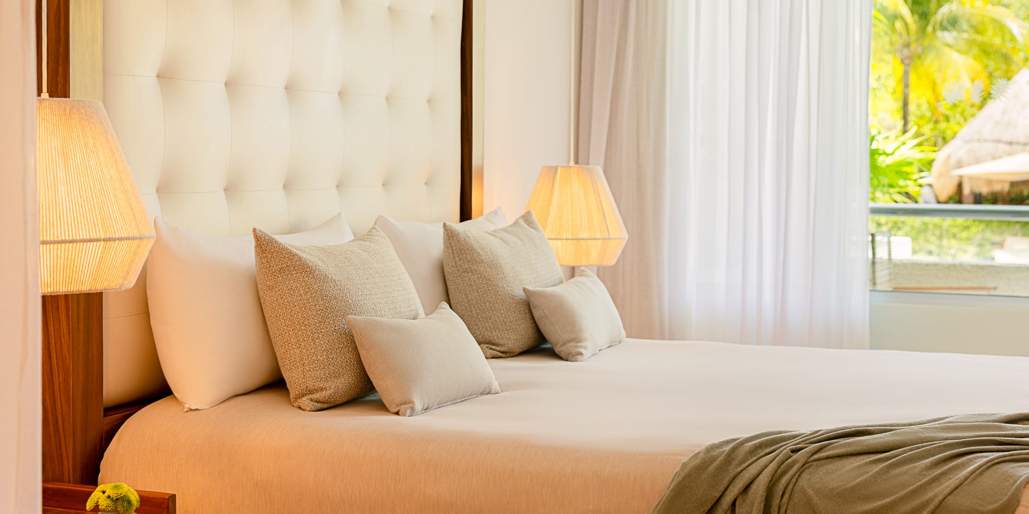 Luxurious king bed hotel room with tufted headboard, warm lamps, and tropical view.
