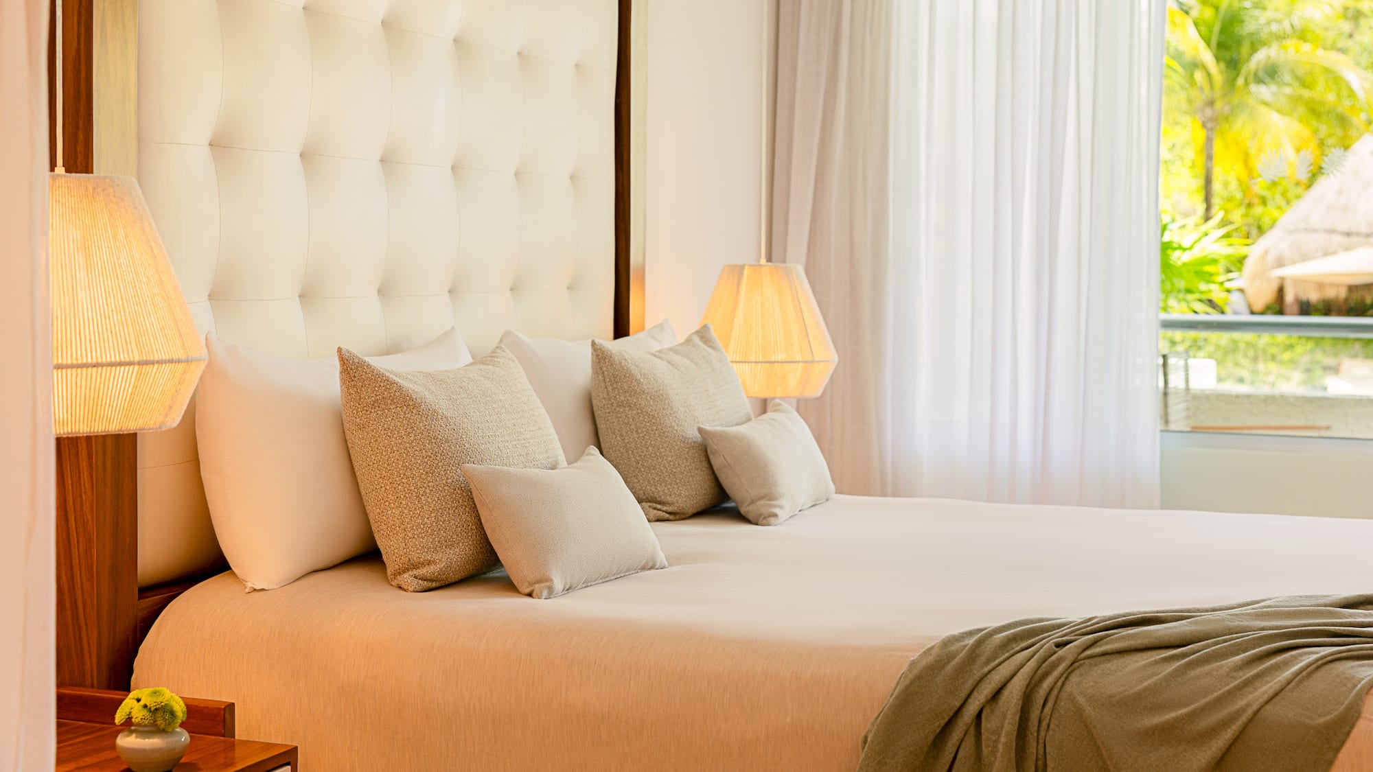 Luxurious king bed hotel room with tufted headboard, warm lamps, and tropical view.