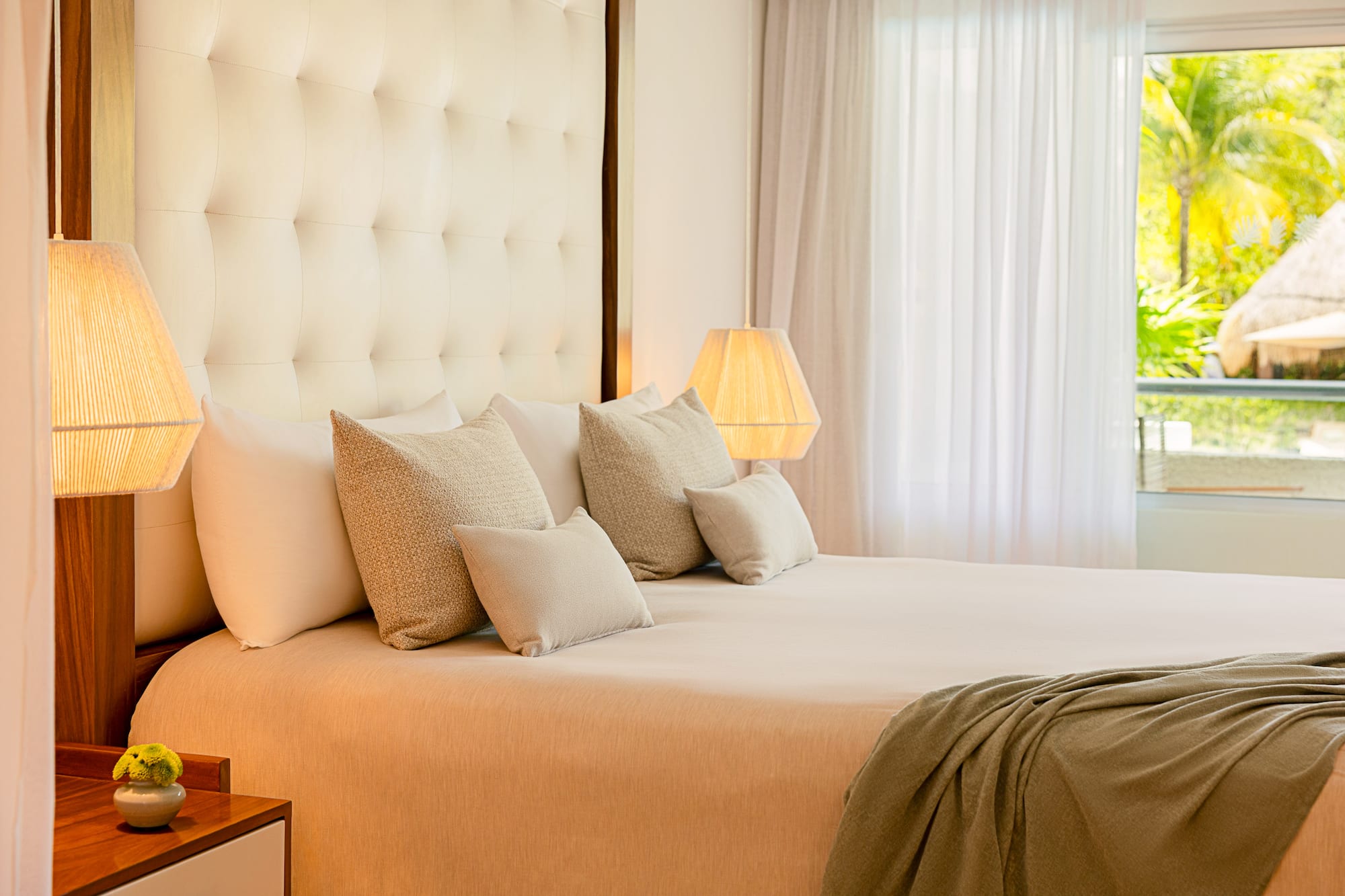 Luxurious king bed hotel room with tufted headboard, warm lamps, and tropical view.