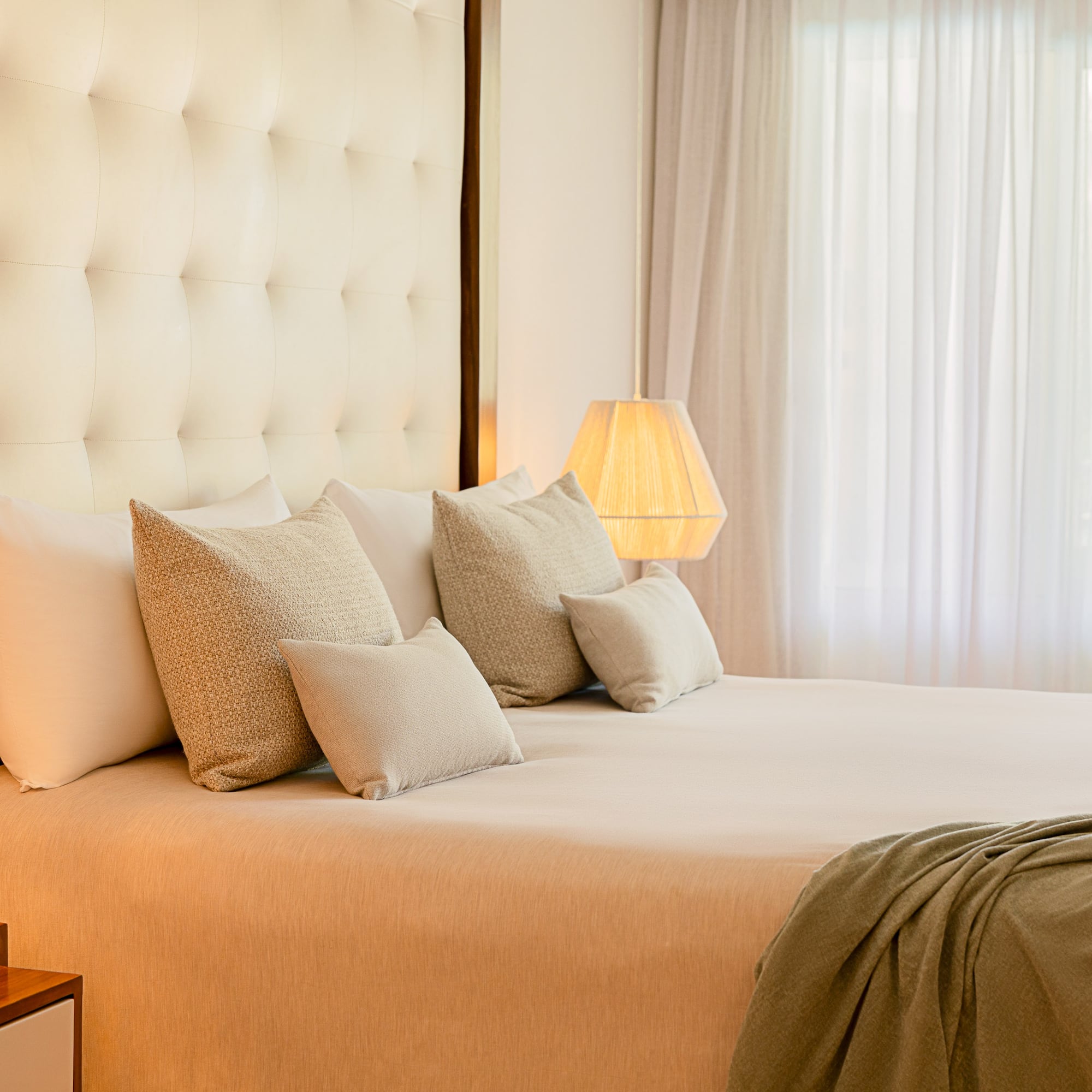 Luxurious king bed hotel room with tufted headboard, warm lamps, and tropical view.