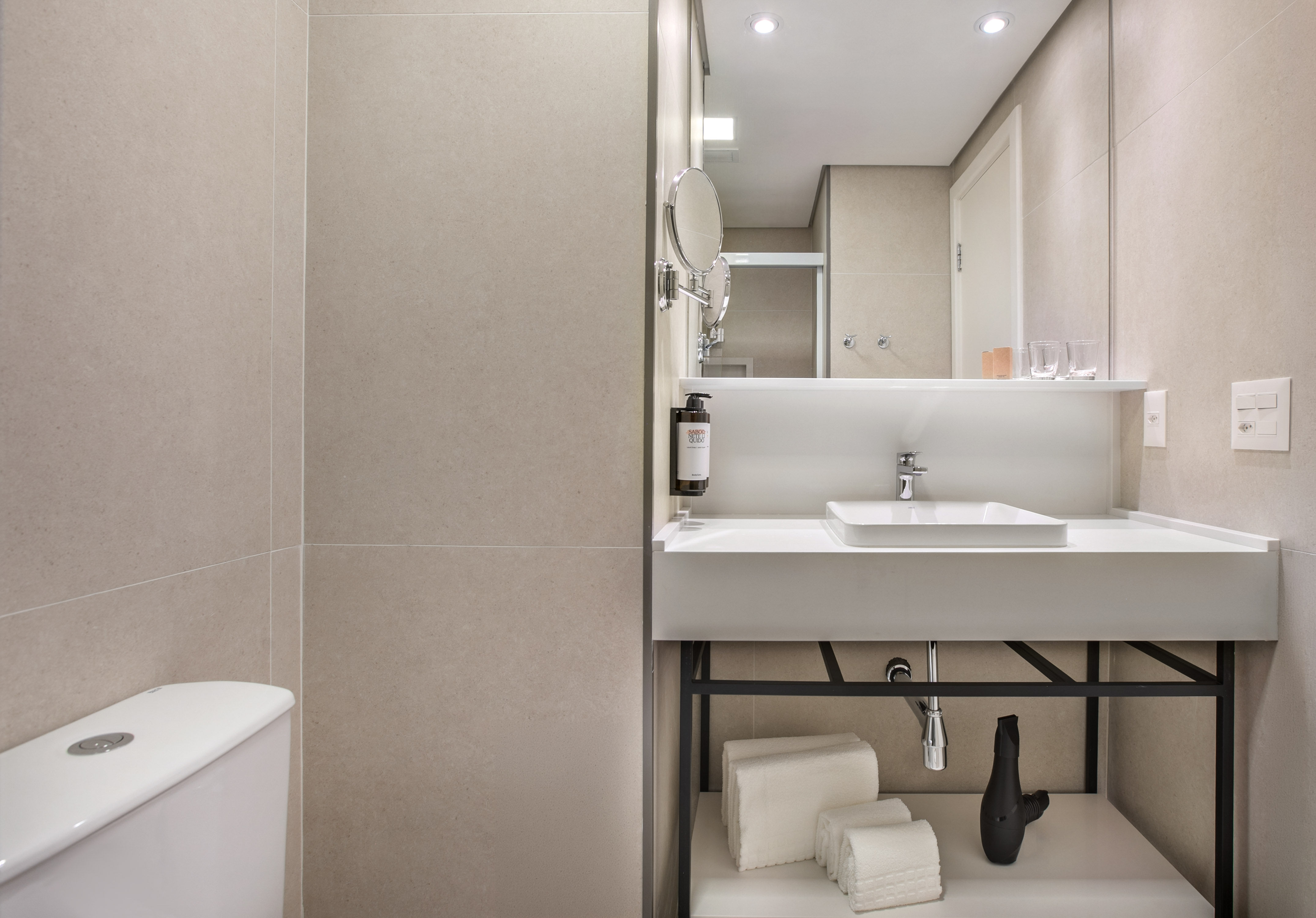 Modern hotel bathroom with white vanity, sink, mirror, and beige tiles.