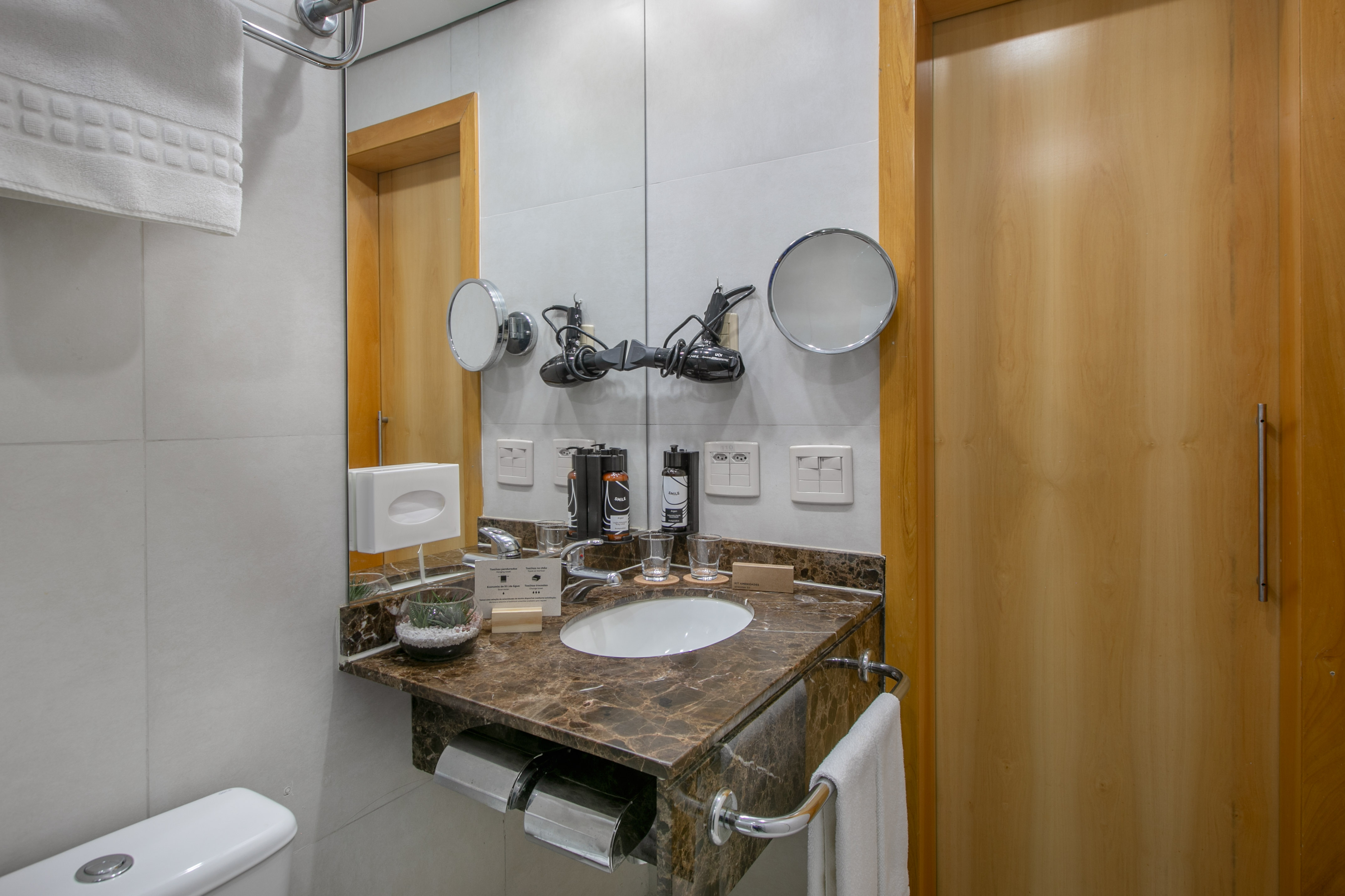 Hotel bathroom with marble vanity, sink, mirrors, hairdryer, and toiletries.
