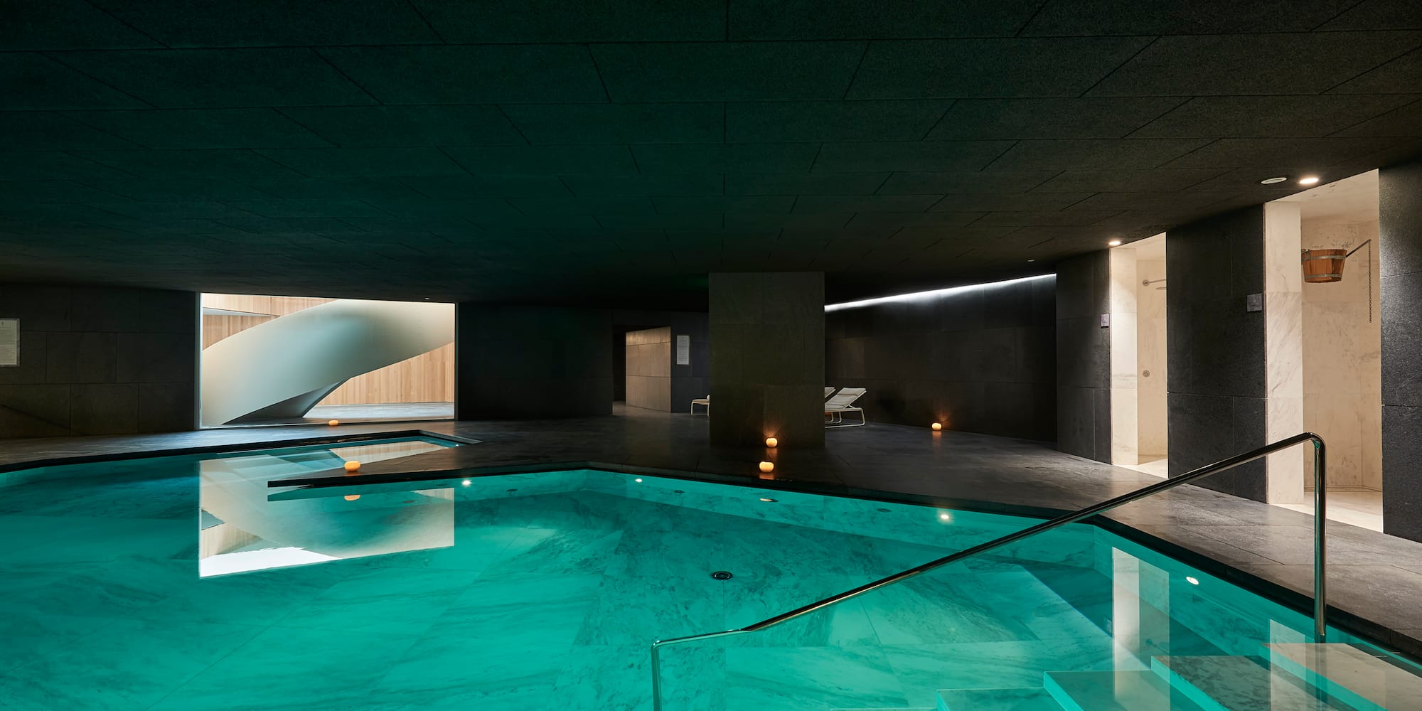 Piscina interior de spa moderno con agua turquesa y escalera de caracol.