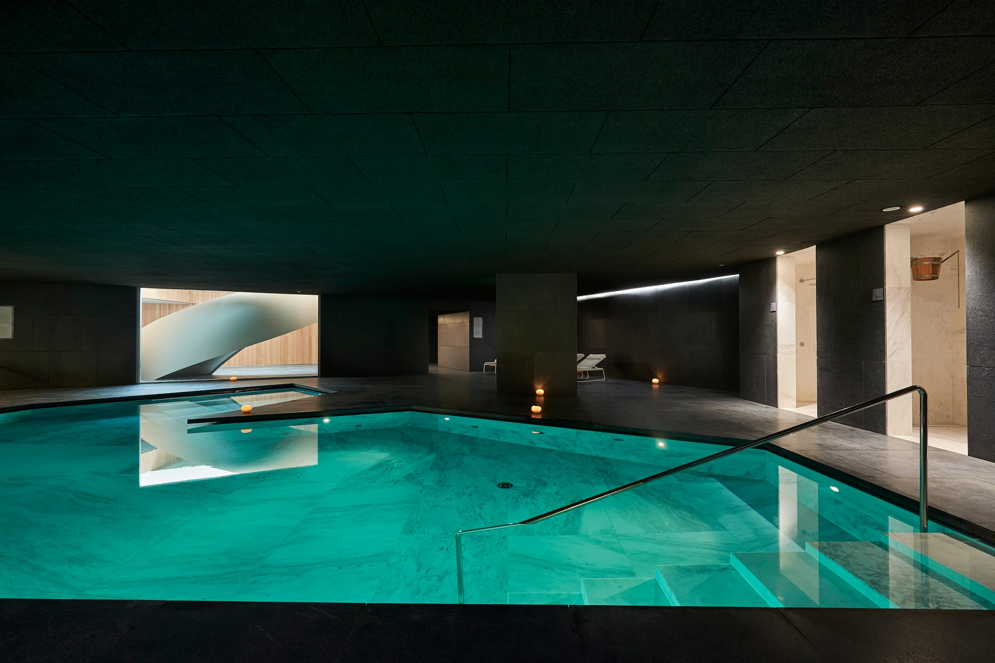 Piscina interior de spa moderno con agua turquesa y escalera de caracol.
