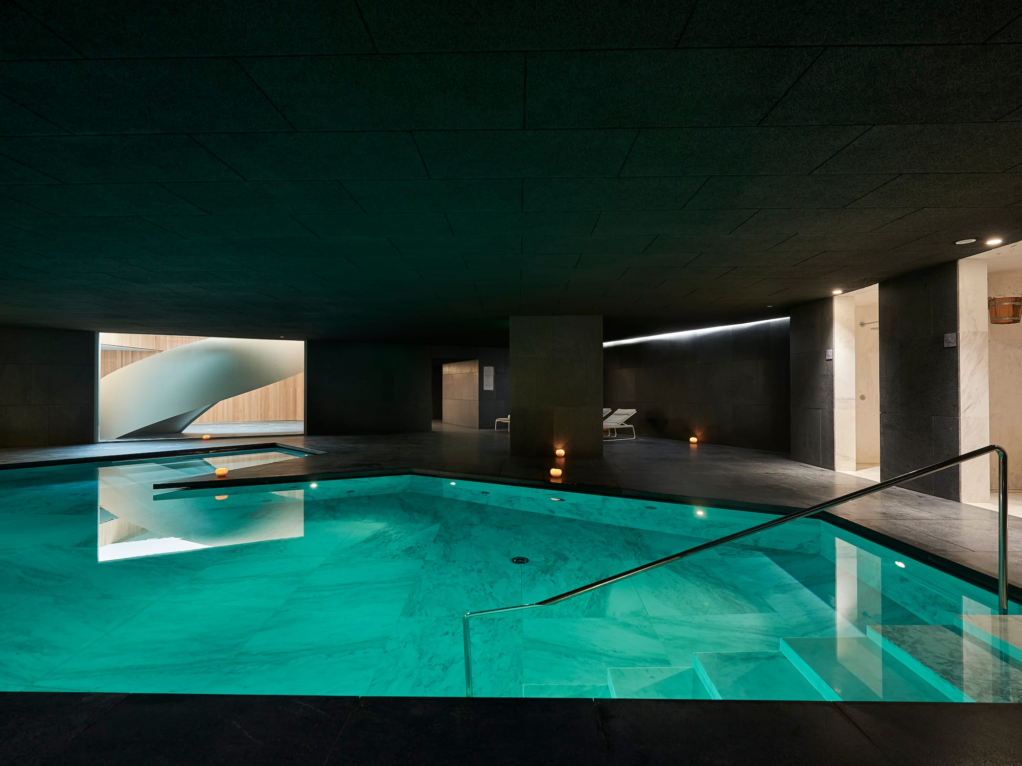 Piscina interior de spa moderno con agua turquesa y escalera de caracol.