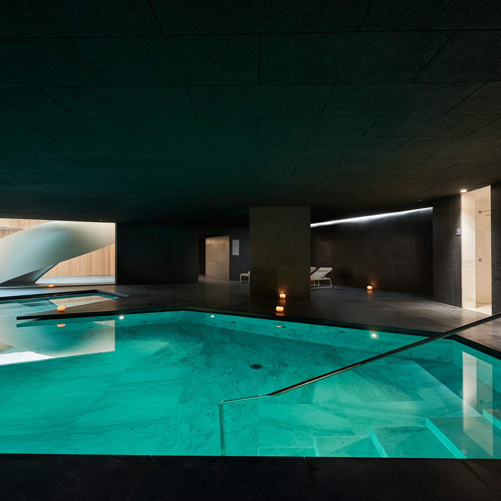 Piscina interior de spa moderno con agua turquesa y escalera de caracol.