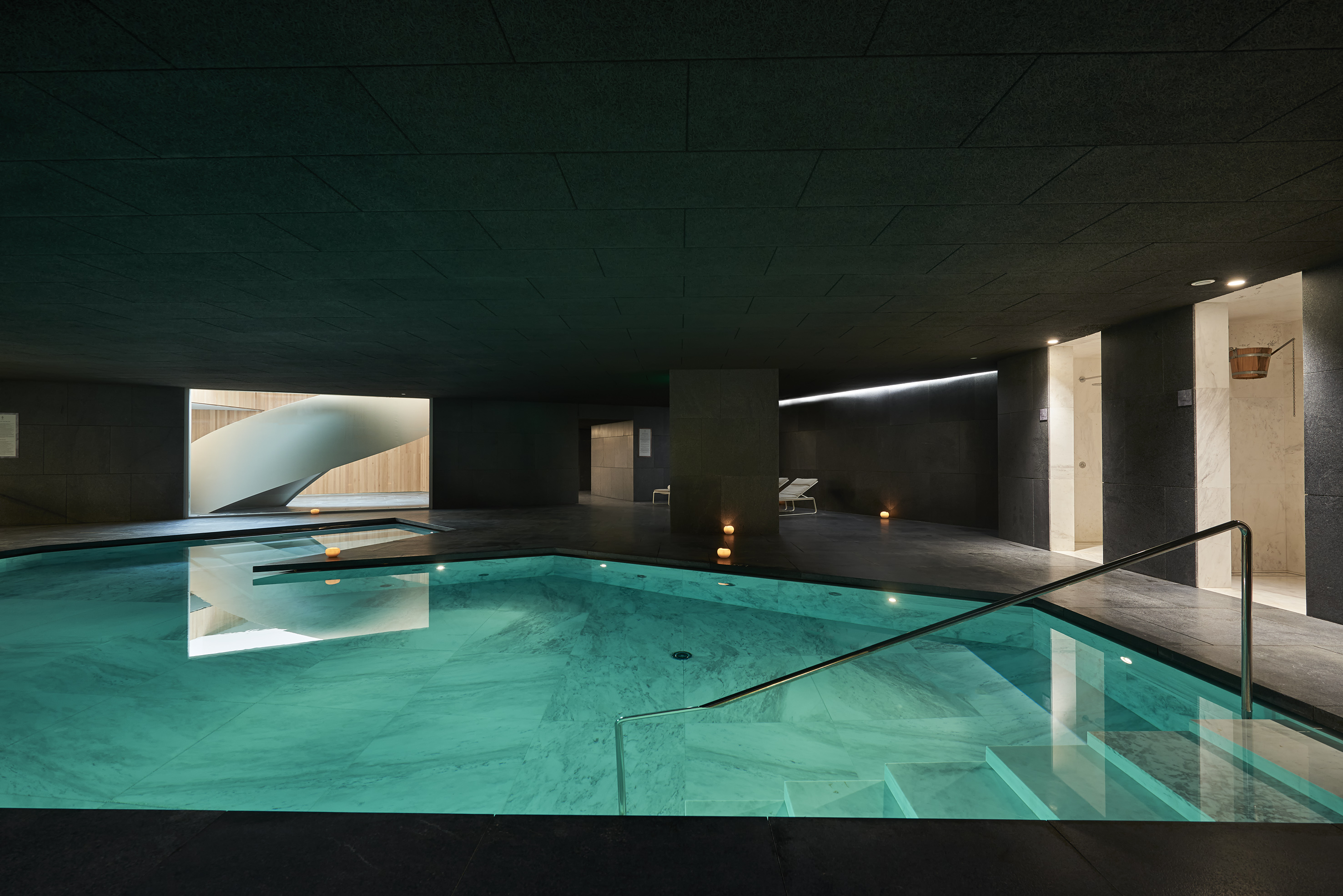 Piscina interior de spa moderno con agua turquesa y escalera de caracol.