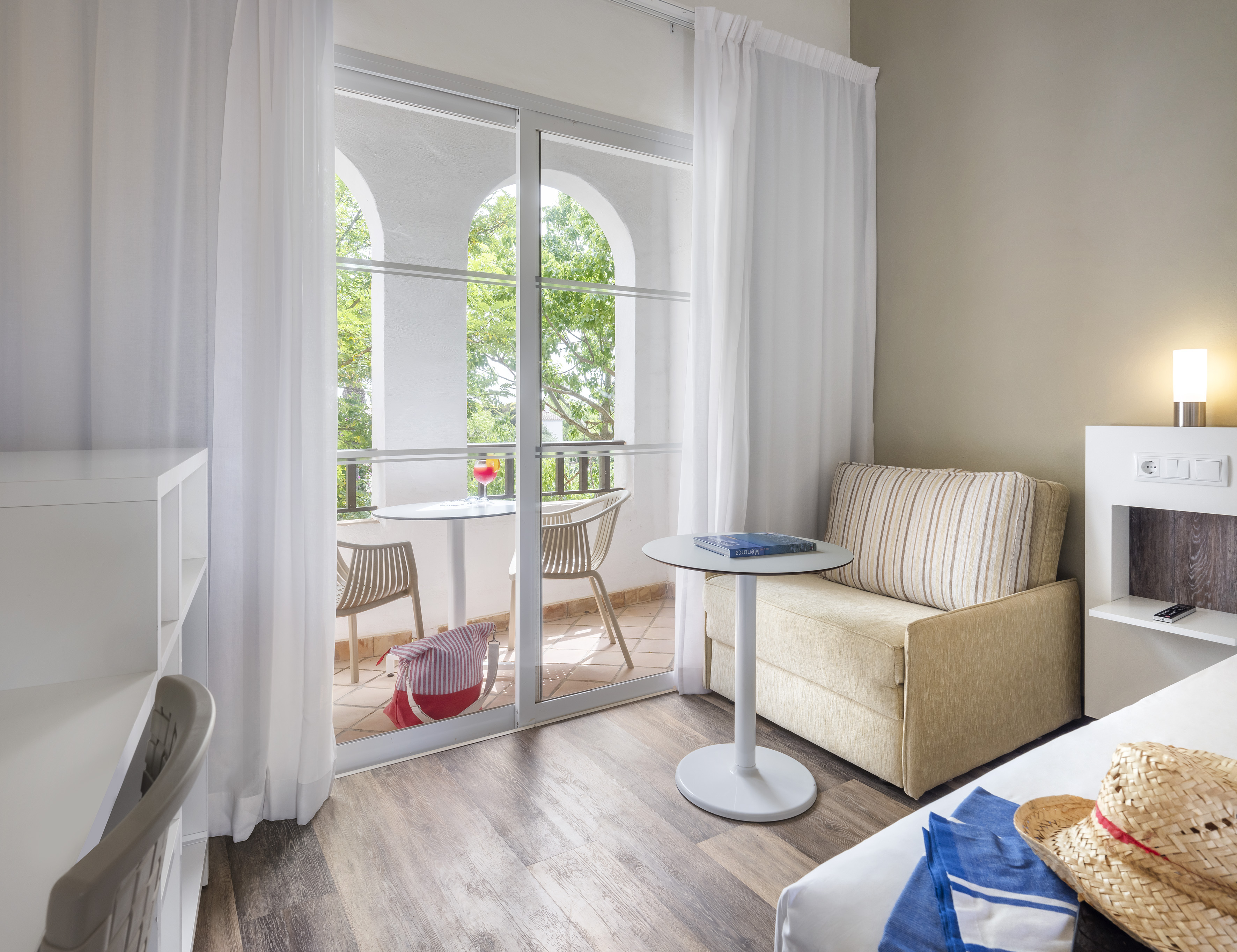 Hotel room with sofa bed, desk, and private balcony with outdoor seating.