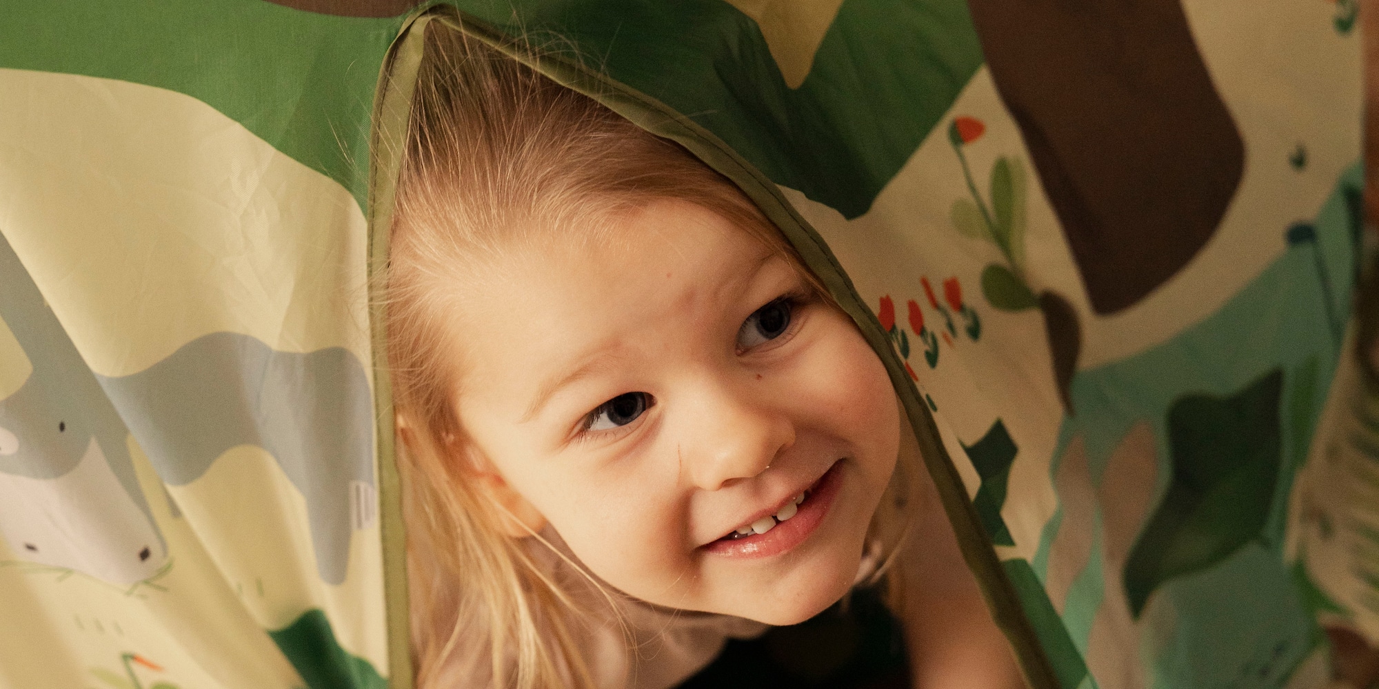 Smiling toddler peeks from colorful jungle play tent during playtime.