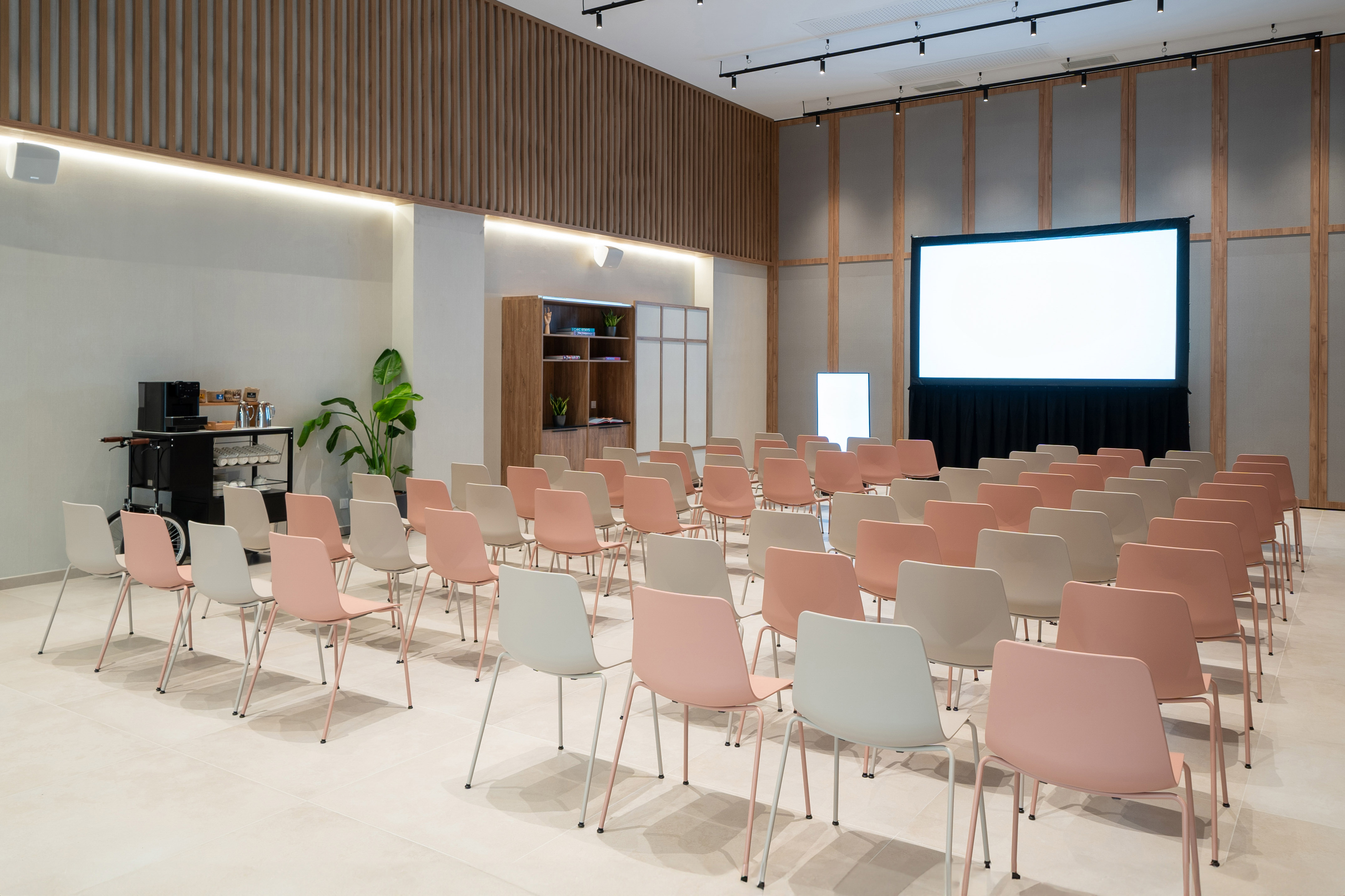 Modern conference room with rows of pink and beige chairs, large screen.