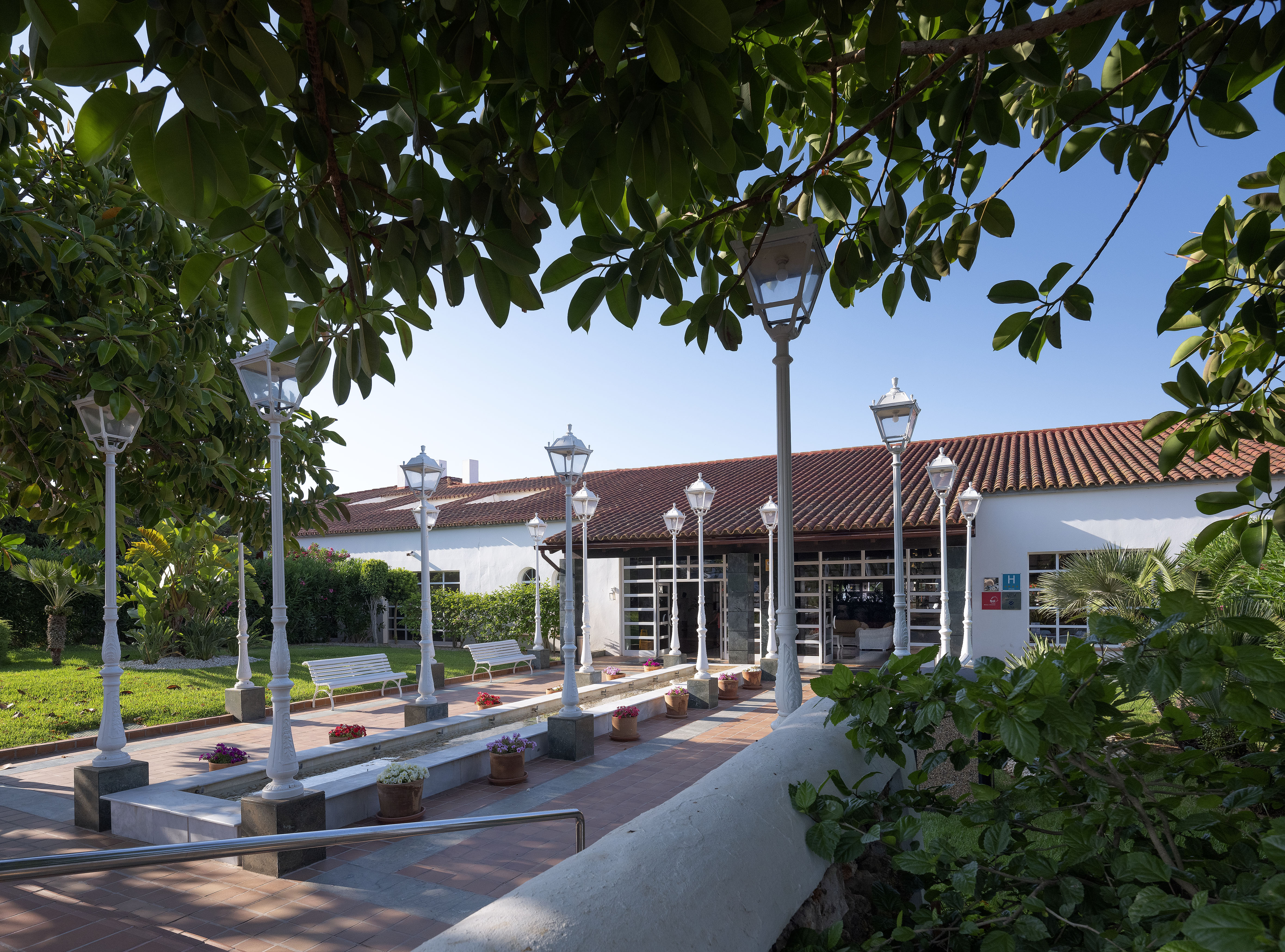Hotel garden pathway with lampposts, tiled roof hotel, and benches.