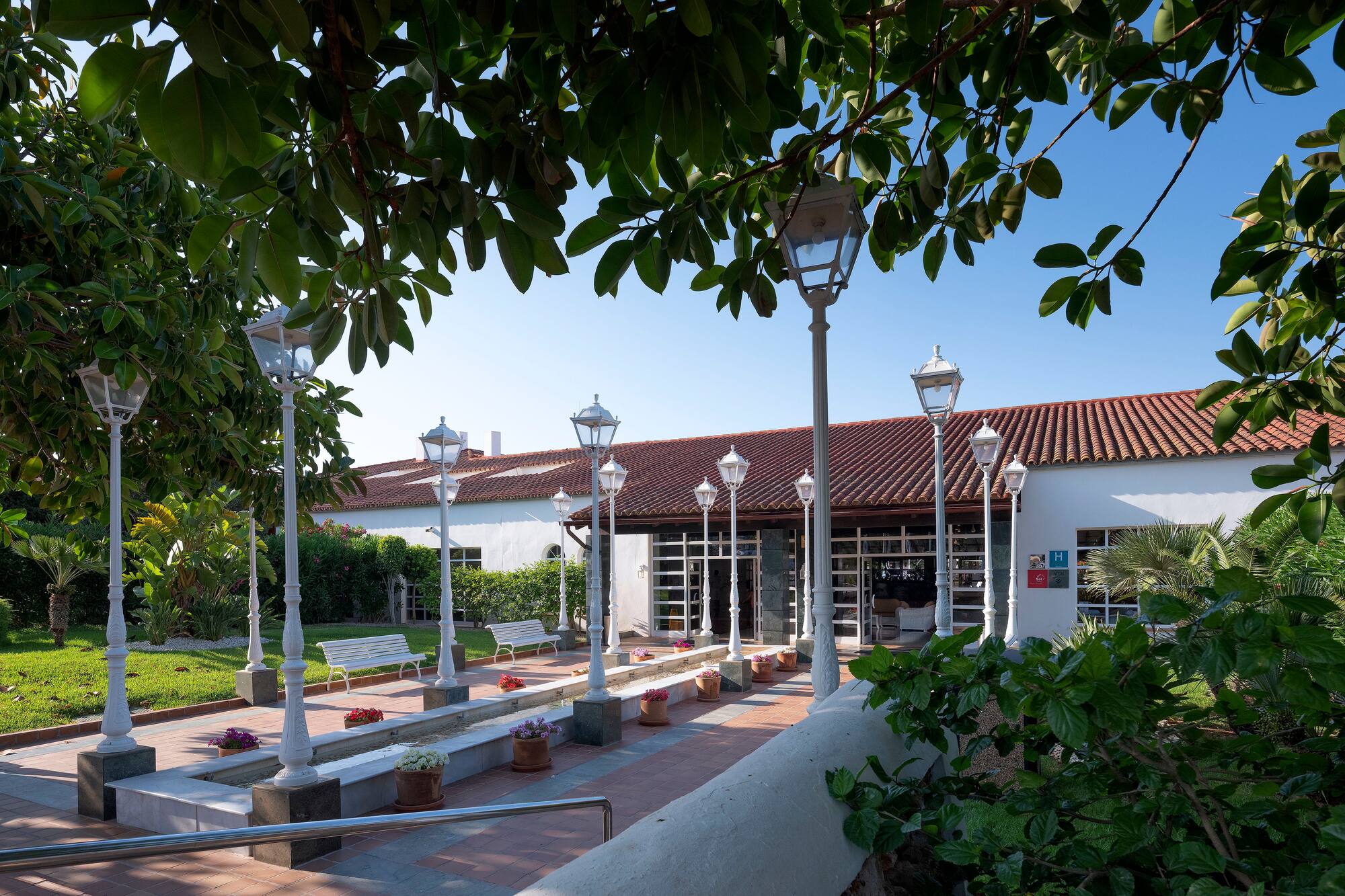 Hotel garden pathway with lampposts, tiled roof hotel, and benches.