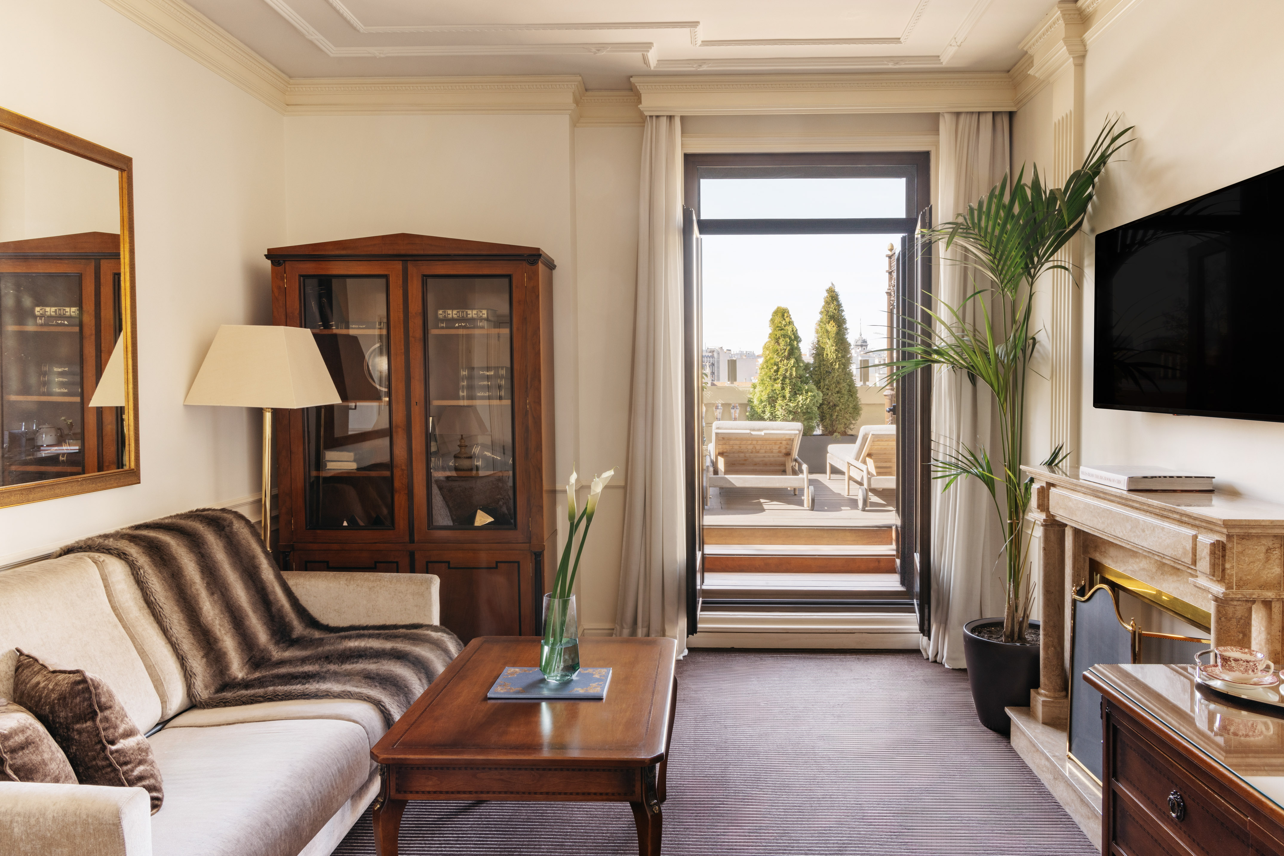 Hotel suite living room with terrace, sofa, wooden cabinet, fireplace, and TV.