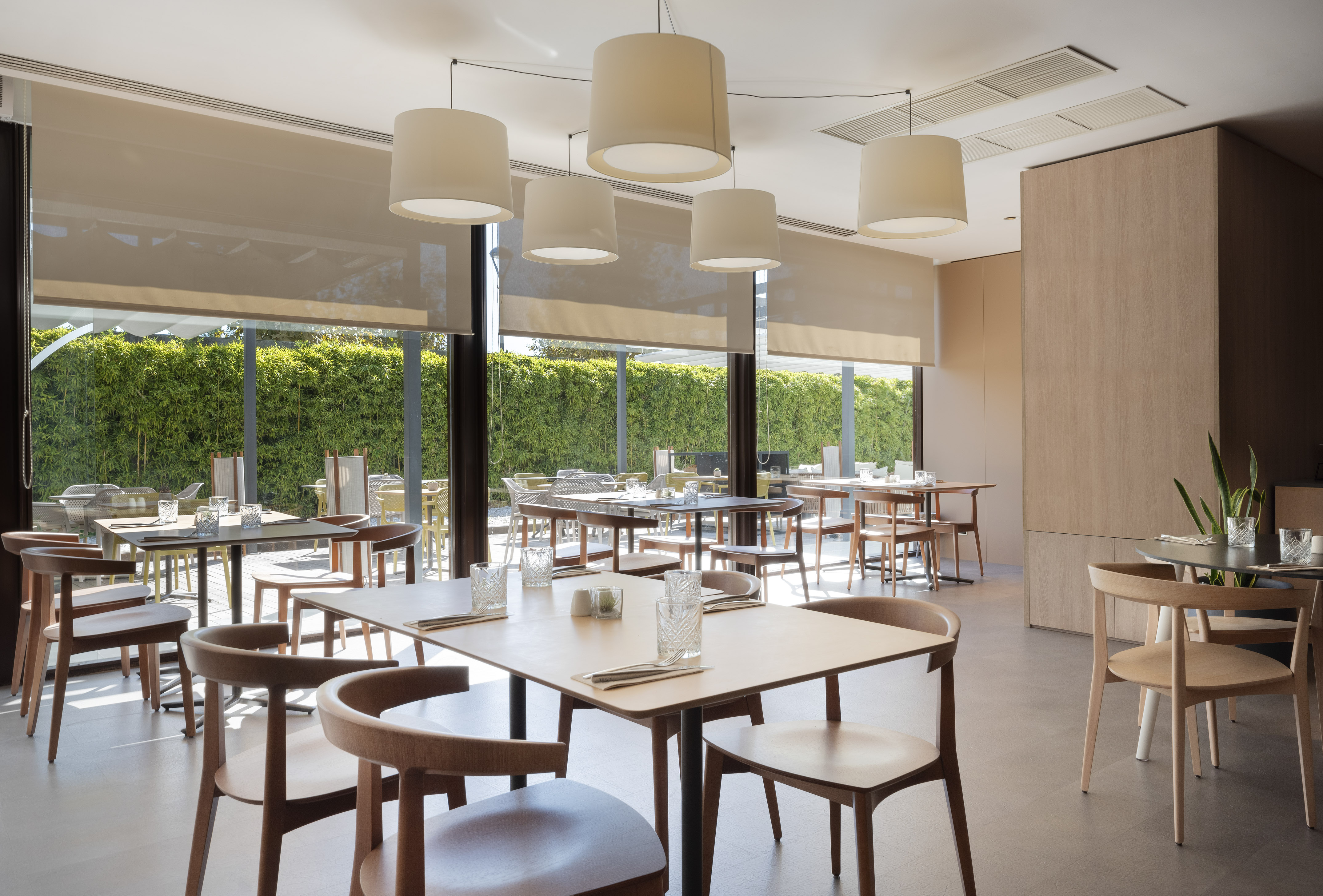 Contemporary restaurant interior with wooden tables, chairs, and large windows.