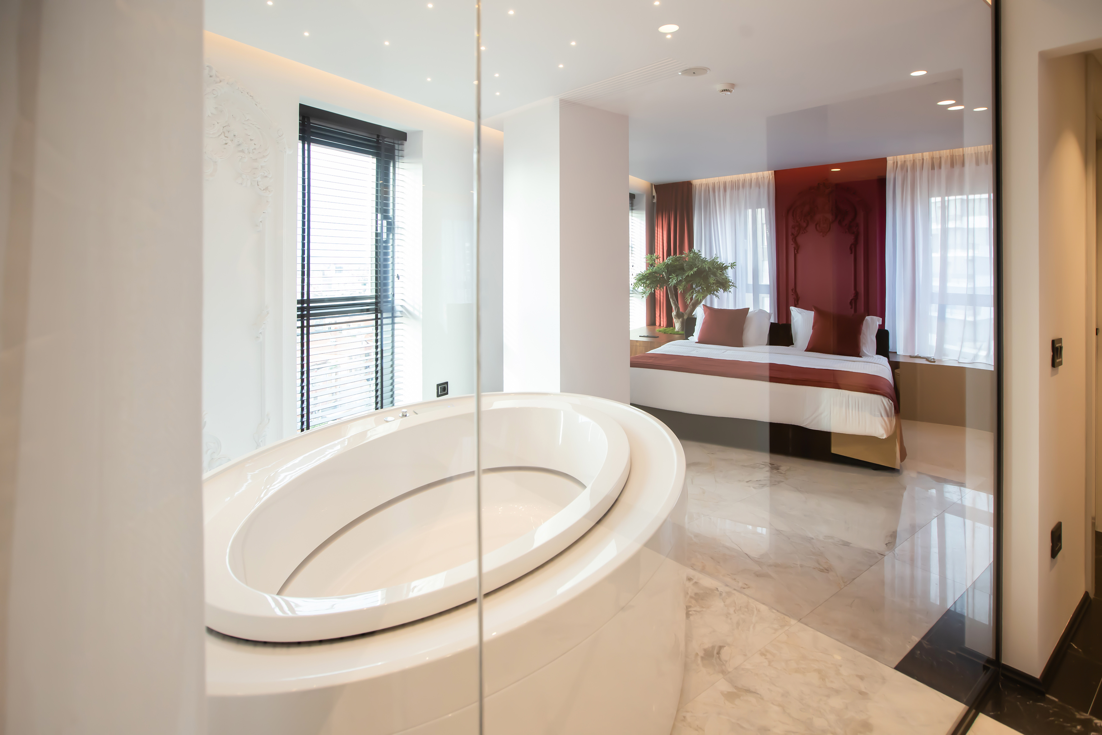 Luxury hotel suite with freestanding bathtub, open bedroom, and red accents.