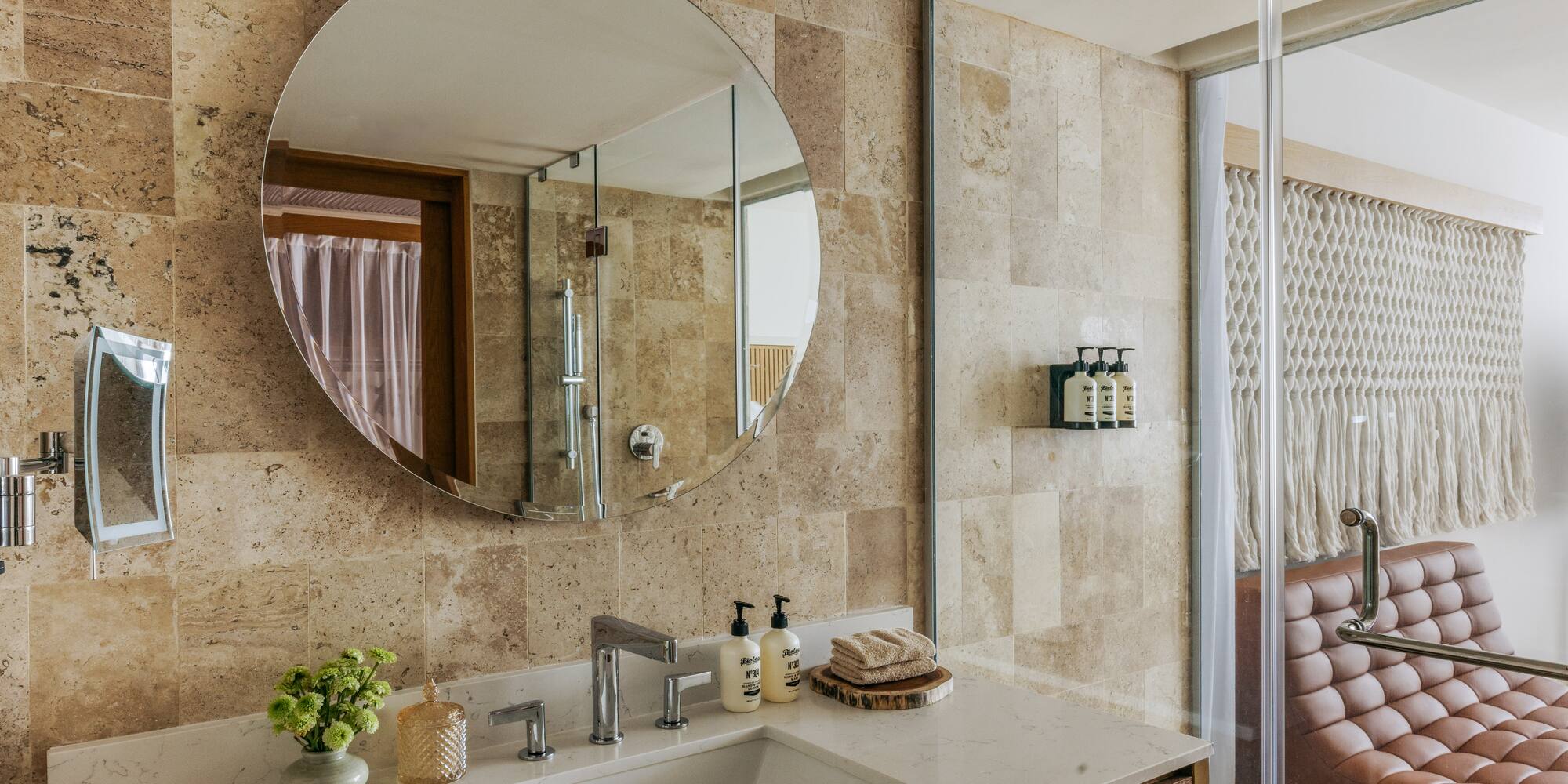 Contemporary bathroom vanity with circular mirror, stone tiles, and glass shower.