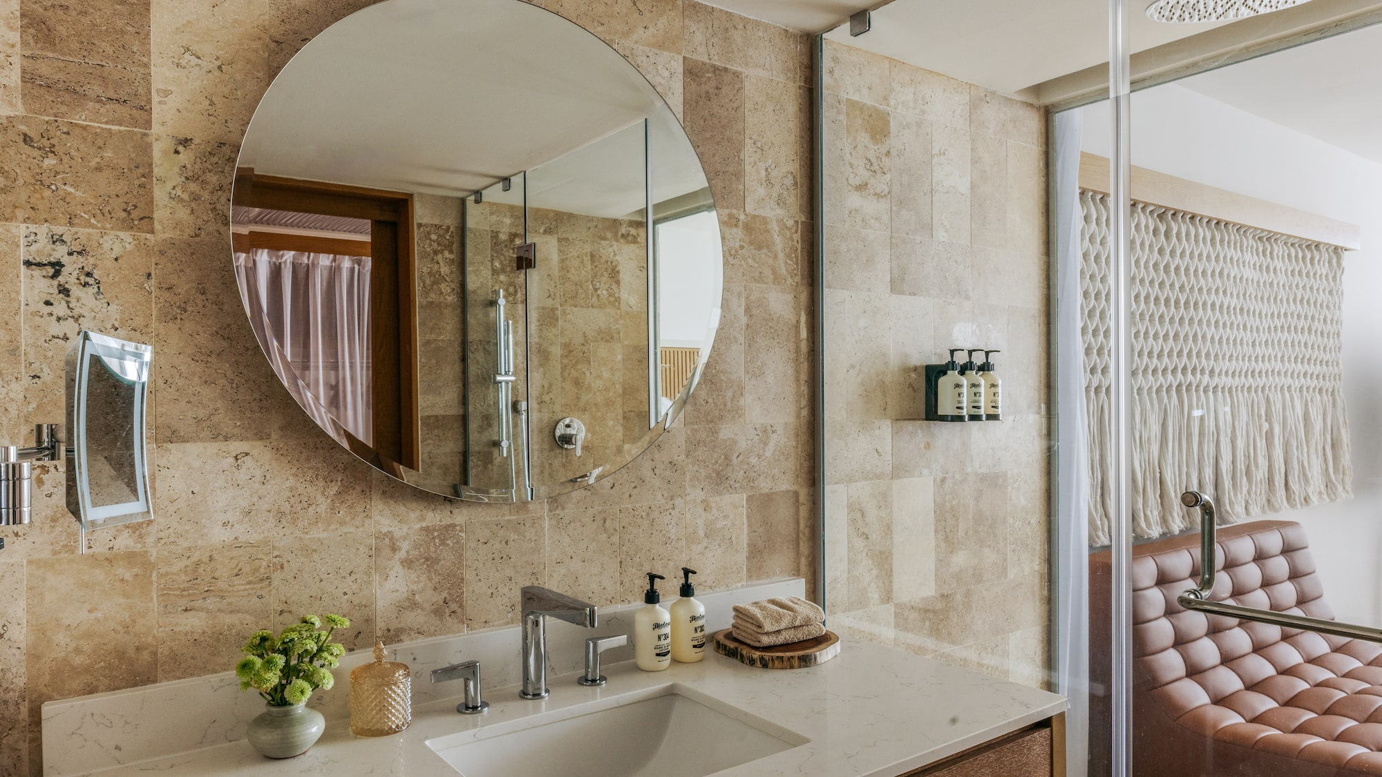 Contemporary bathroom vanity with circular mirror, stone tiles, and glass shower.