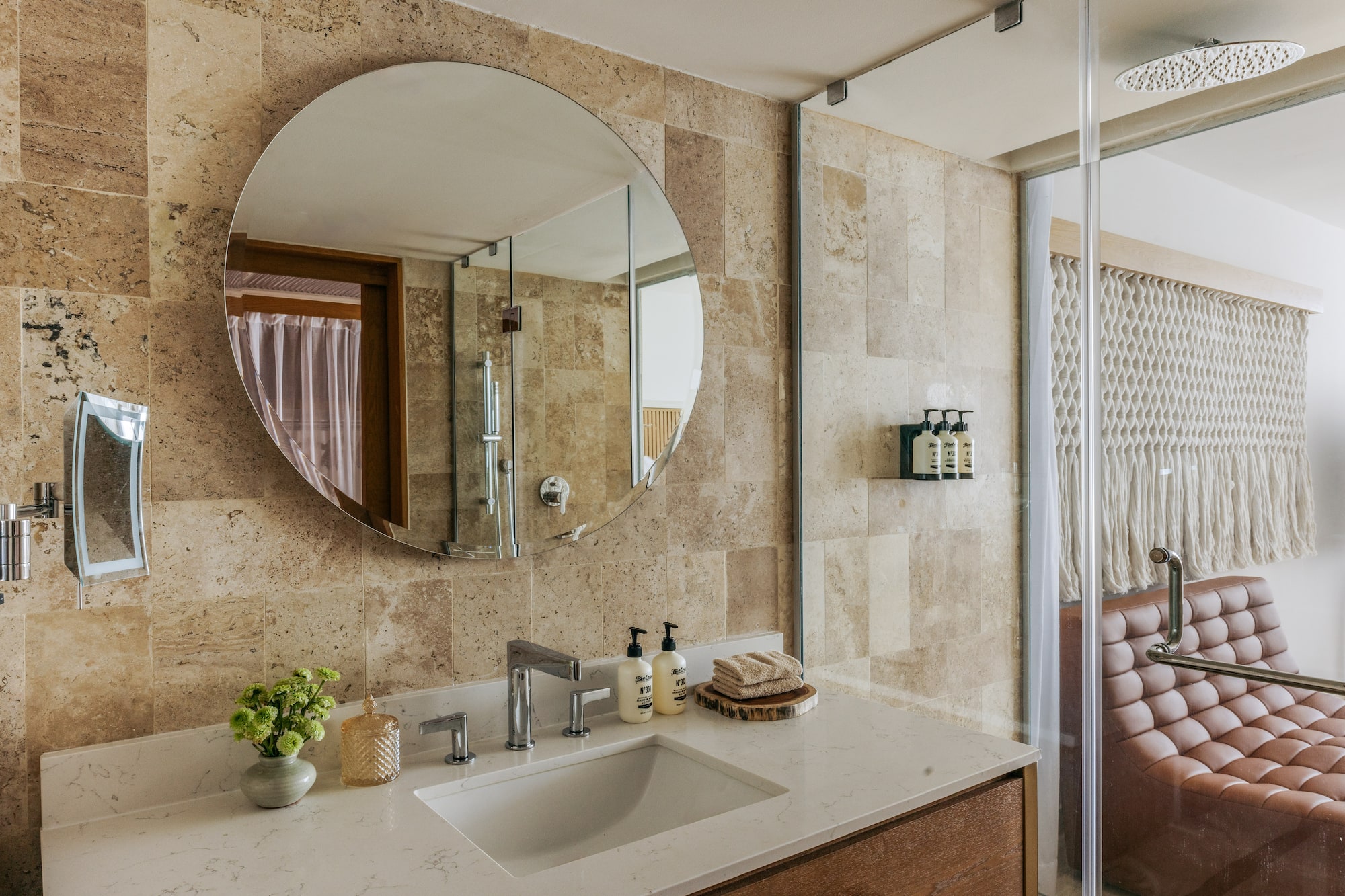Contemporary bathroom vanity with circular mirror, stone tiles, and glass shower.